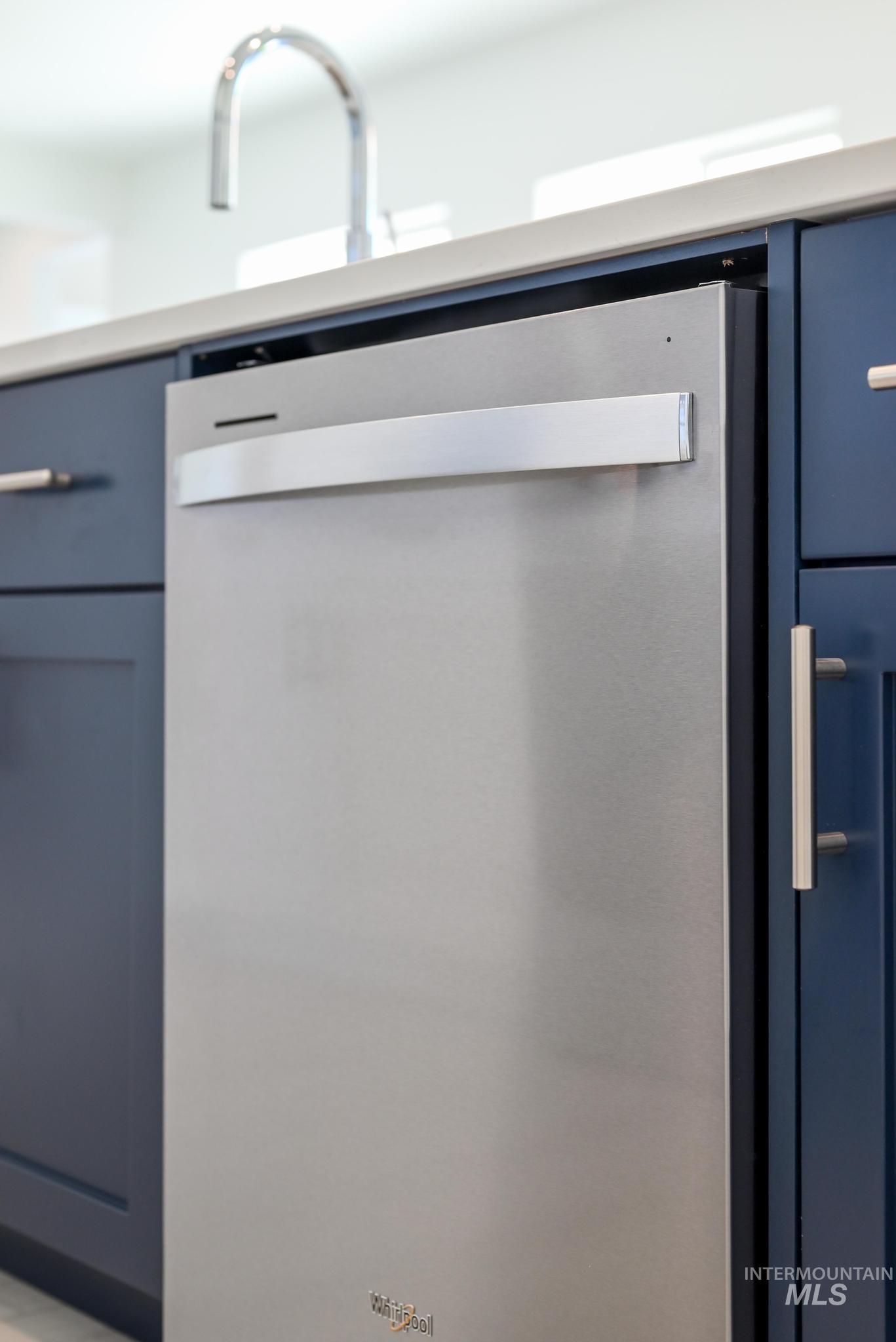 Kitchen view of blue cabinetry, stainless steel dishwasher, and light countertops