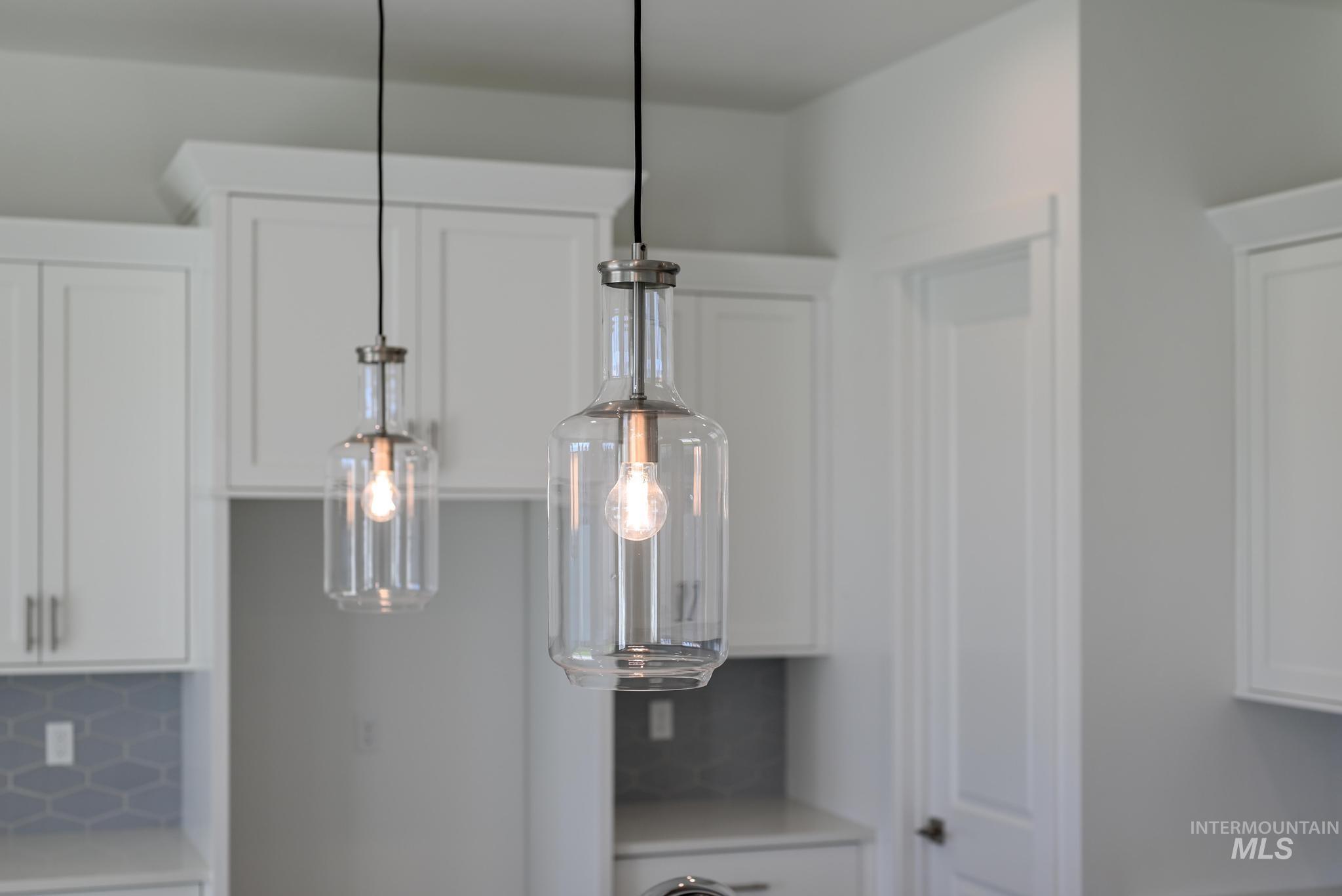 Kitchen view of white cabinetry, hanging light fixtures, and backsplash
