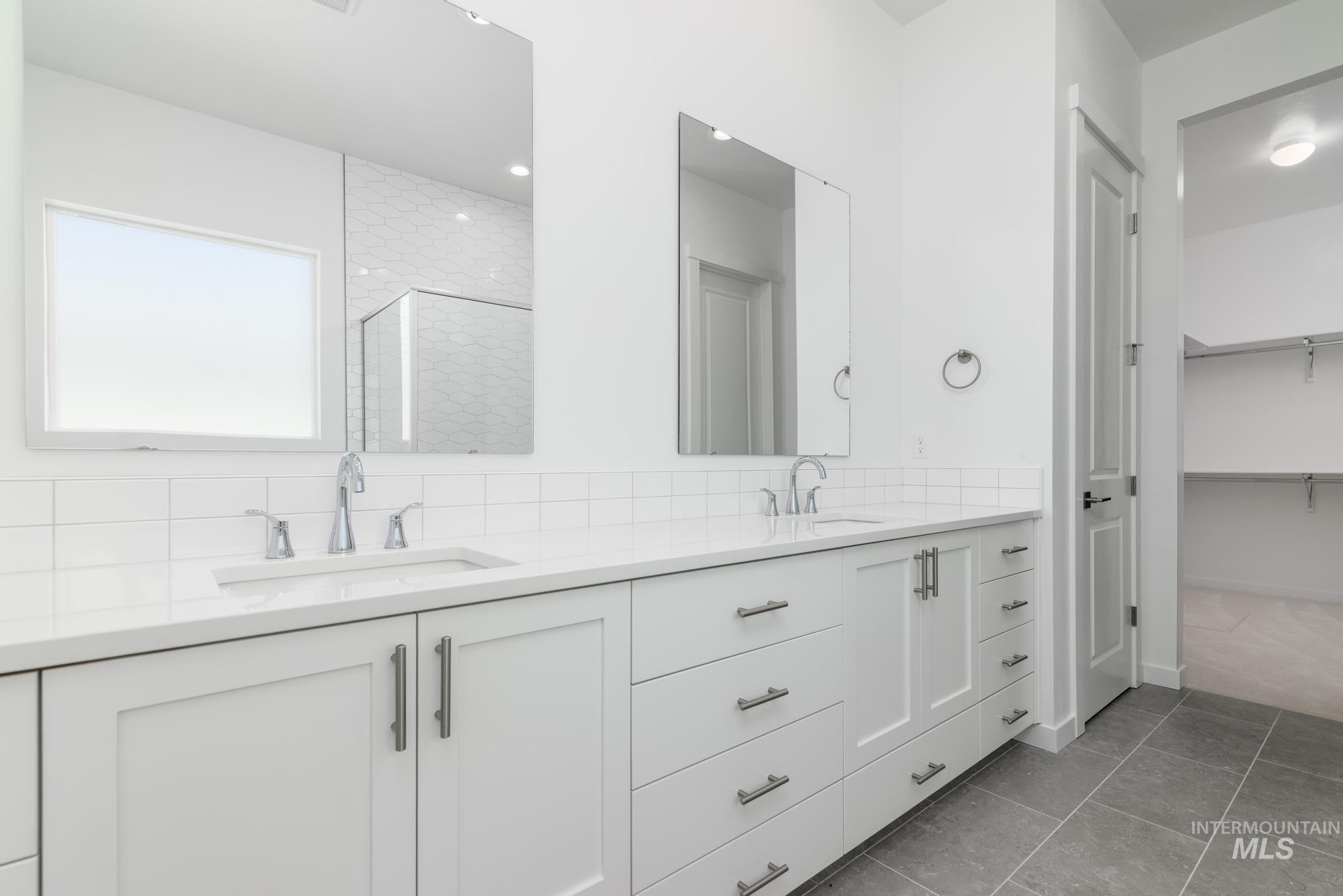 Bathroom with a shower stall, double vanity, a spacious closet, decorative backsplash, and light tile patterned flooring