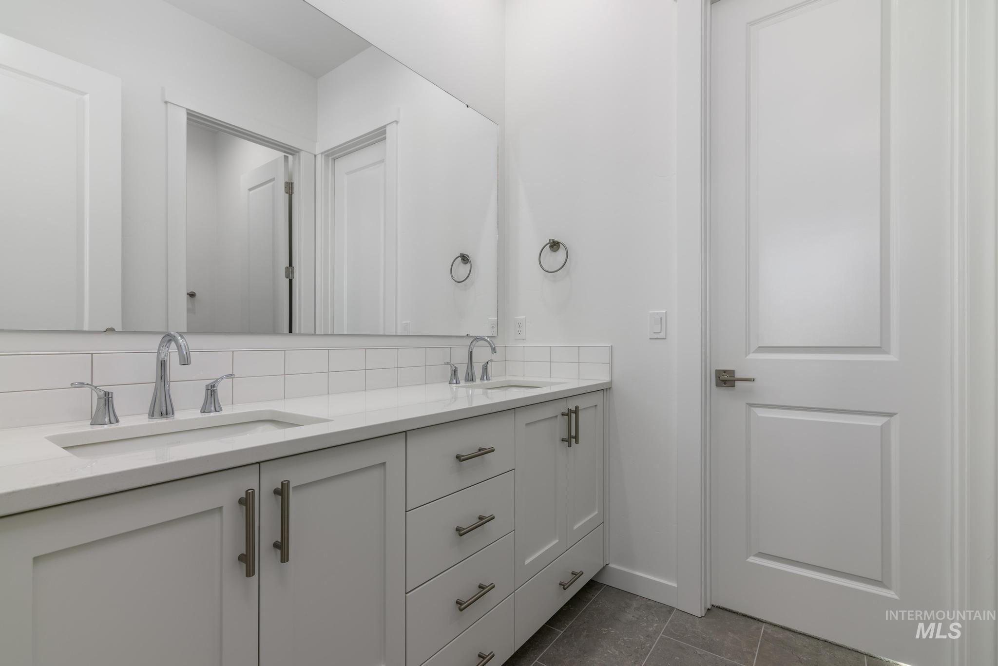 Full bath featuring double vanity, tasteful backsplash, and dark tile patterned flooring
