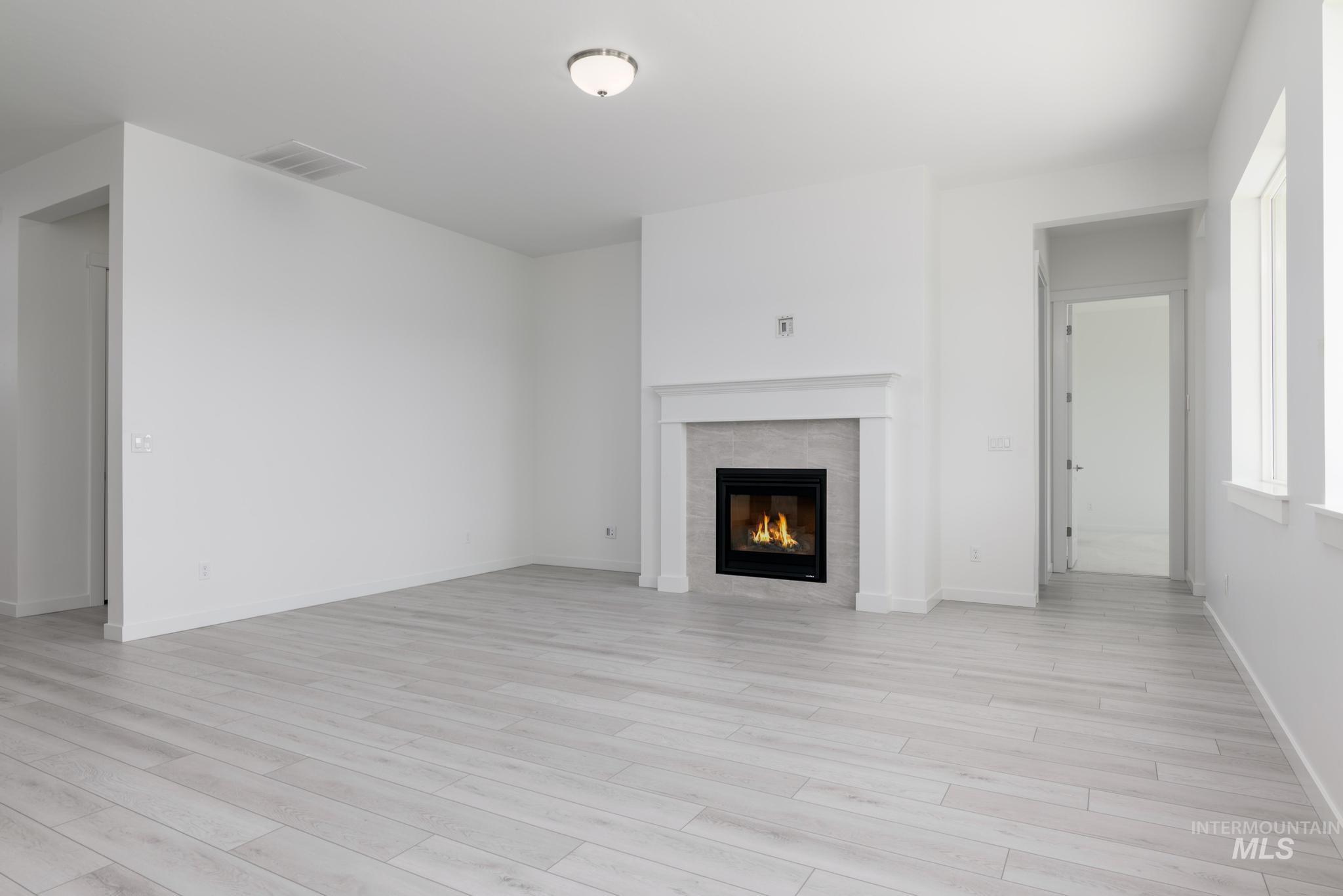 Unfurnished living room featuring a tiled fireplace and light wood finished floors