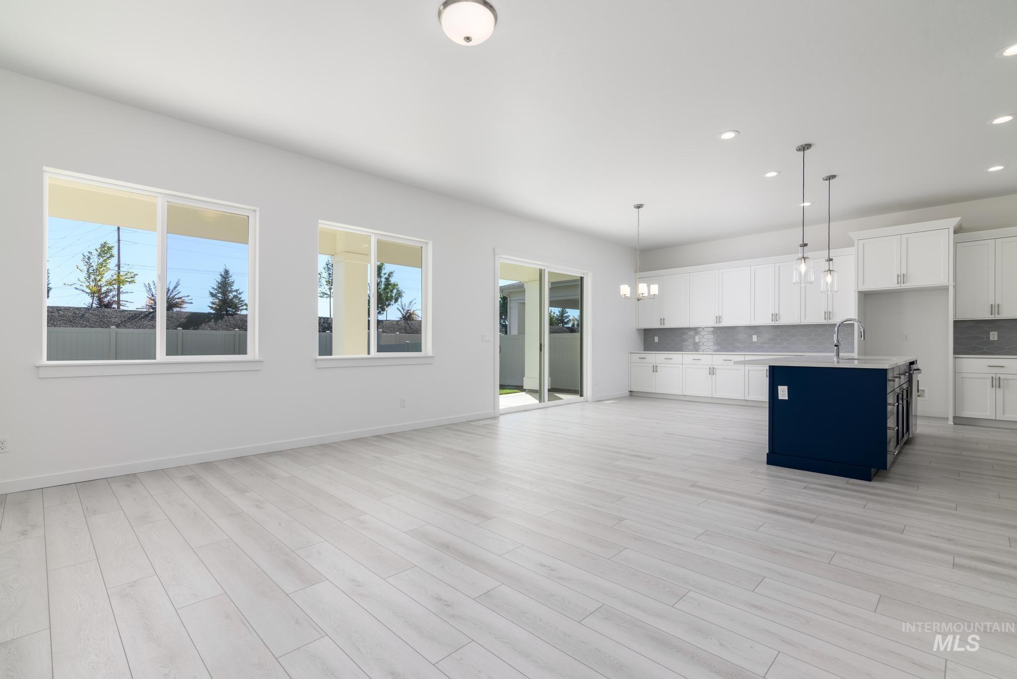 Kitchen featuring white cabinetry, an island with sink, decorative light fixtures, backsplash, and open floor plan