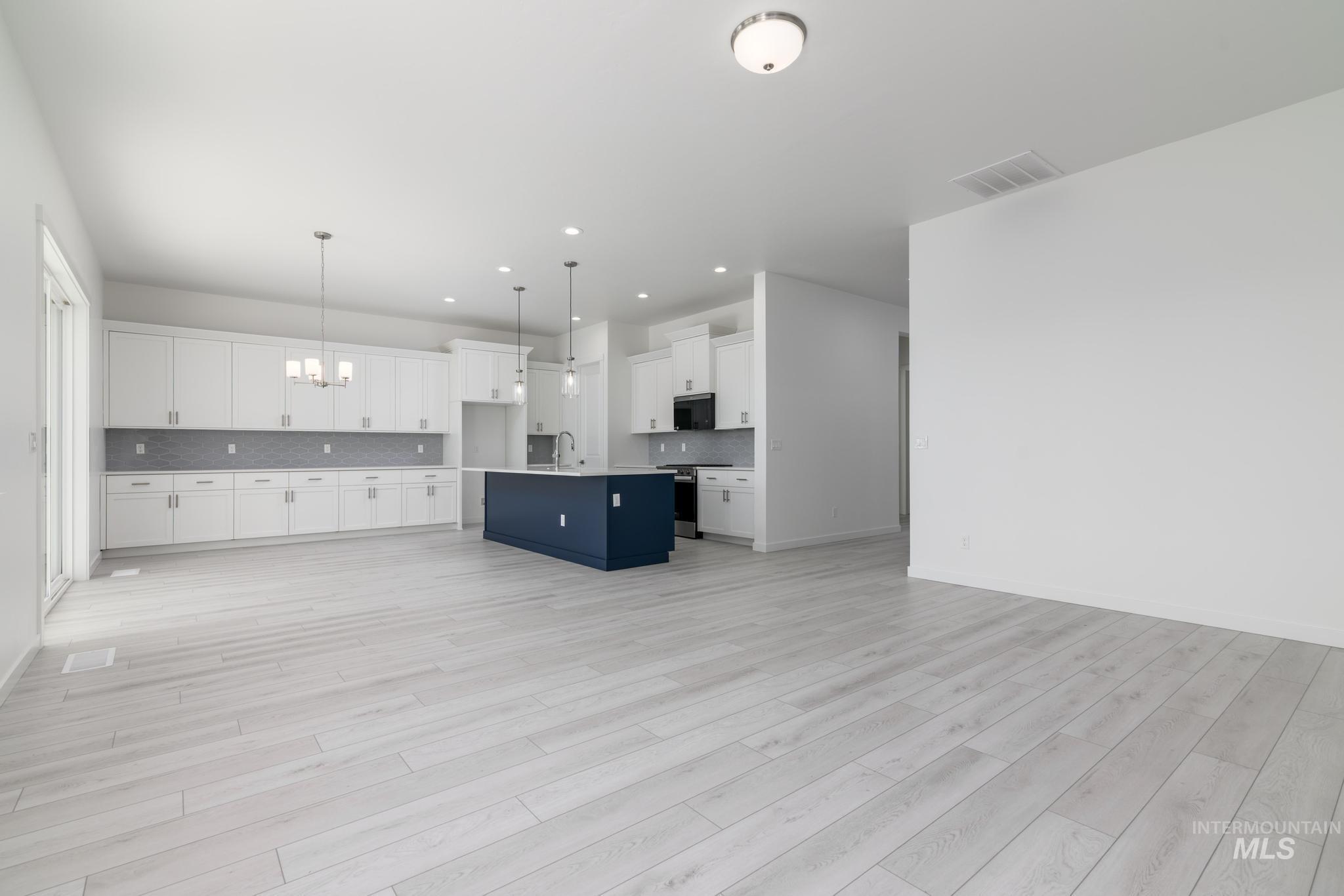 Kitchen featuring open floor plan, white cabinets, a chandelier, an island with sink, and tasteful backsplash