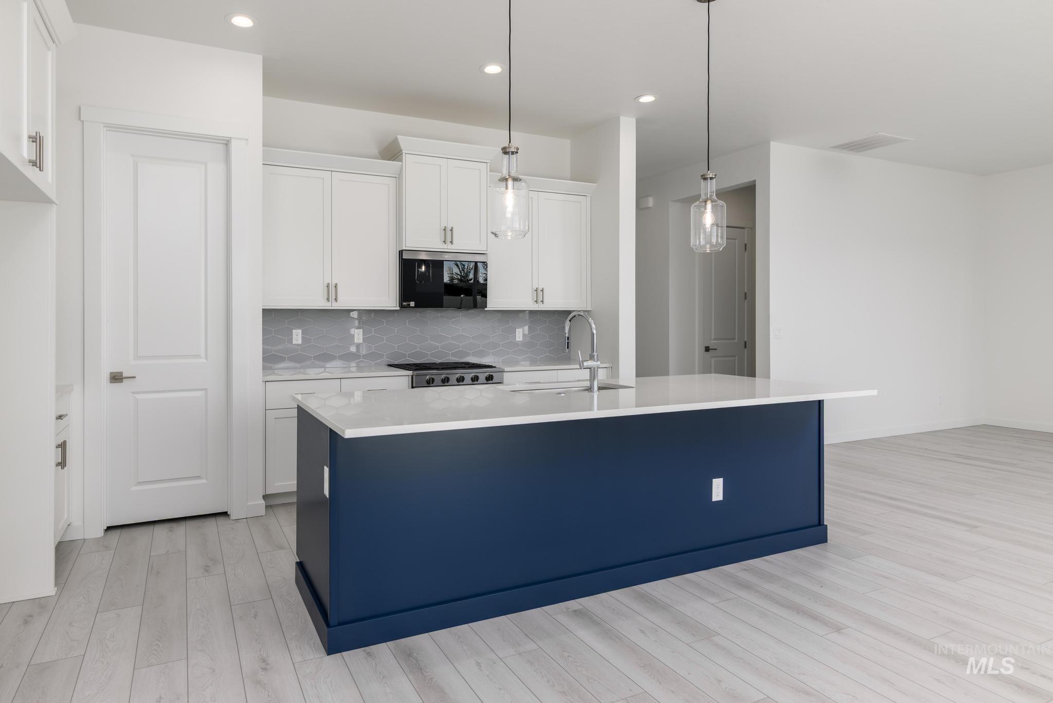 Kitchen with white cabinets, backsplash, decorative light fixtures, an island with sink, and recessed lighting