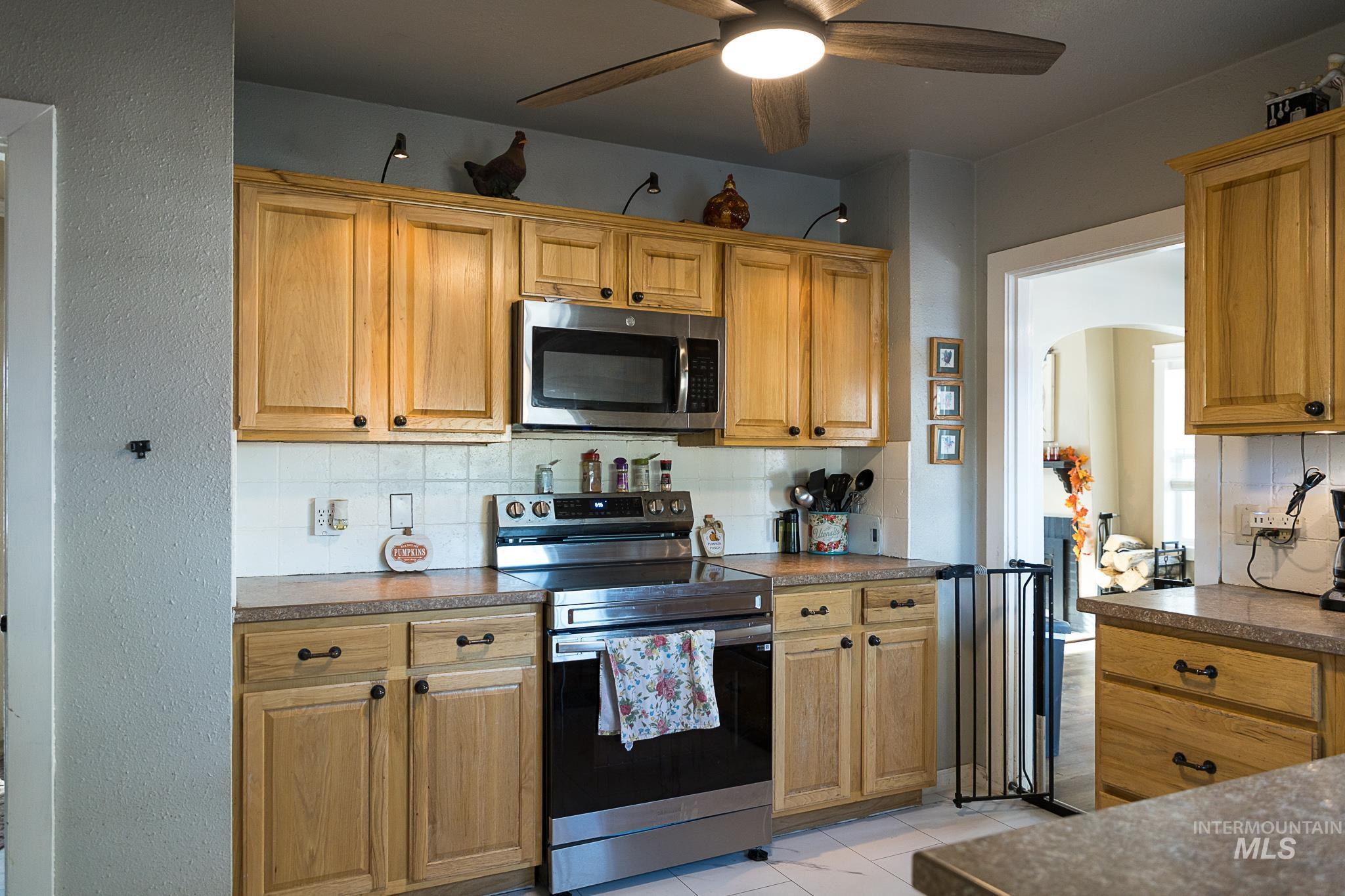 Kitchen featuring backsplash, stainless steel appliances, ceiling fan, a textured wall, and dark countertops