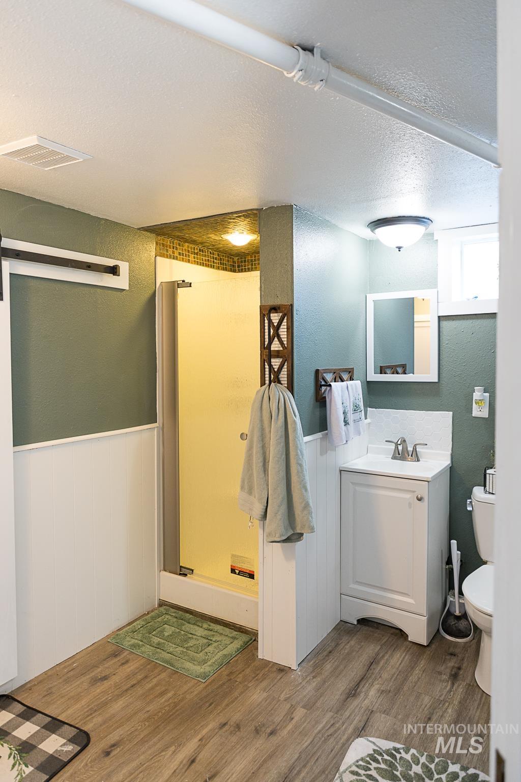 Bathroom with a textured ceiling, a textured wall, vanity, a shower stall, and wood finished floors