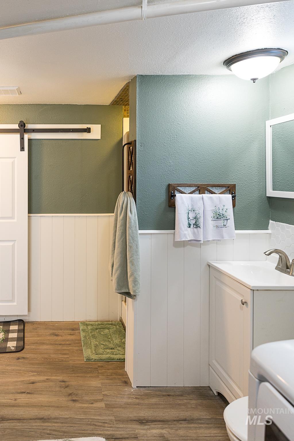 Bathroom featuring a textured wall, wood finished floors, vanity, a wainscoted wall, and a textured ceiling
