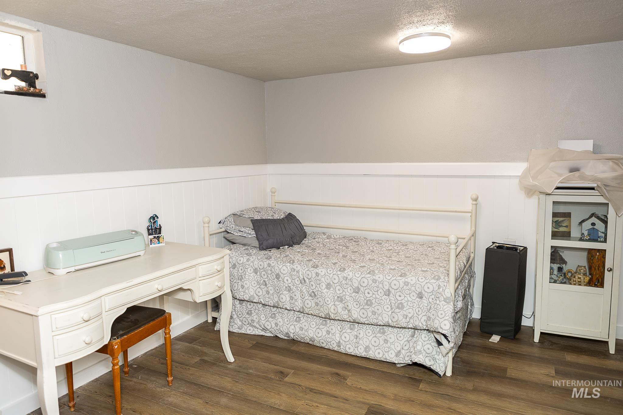 Bedroom featuring a textured ceiling, a wainscoted wall, and dark wood finished floors