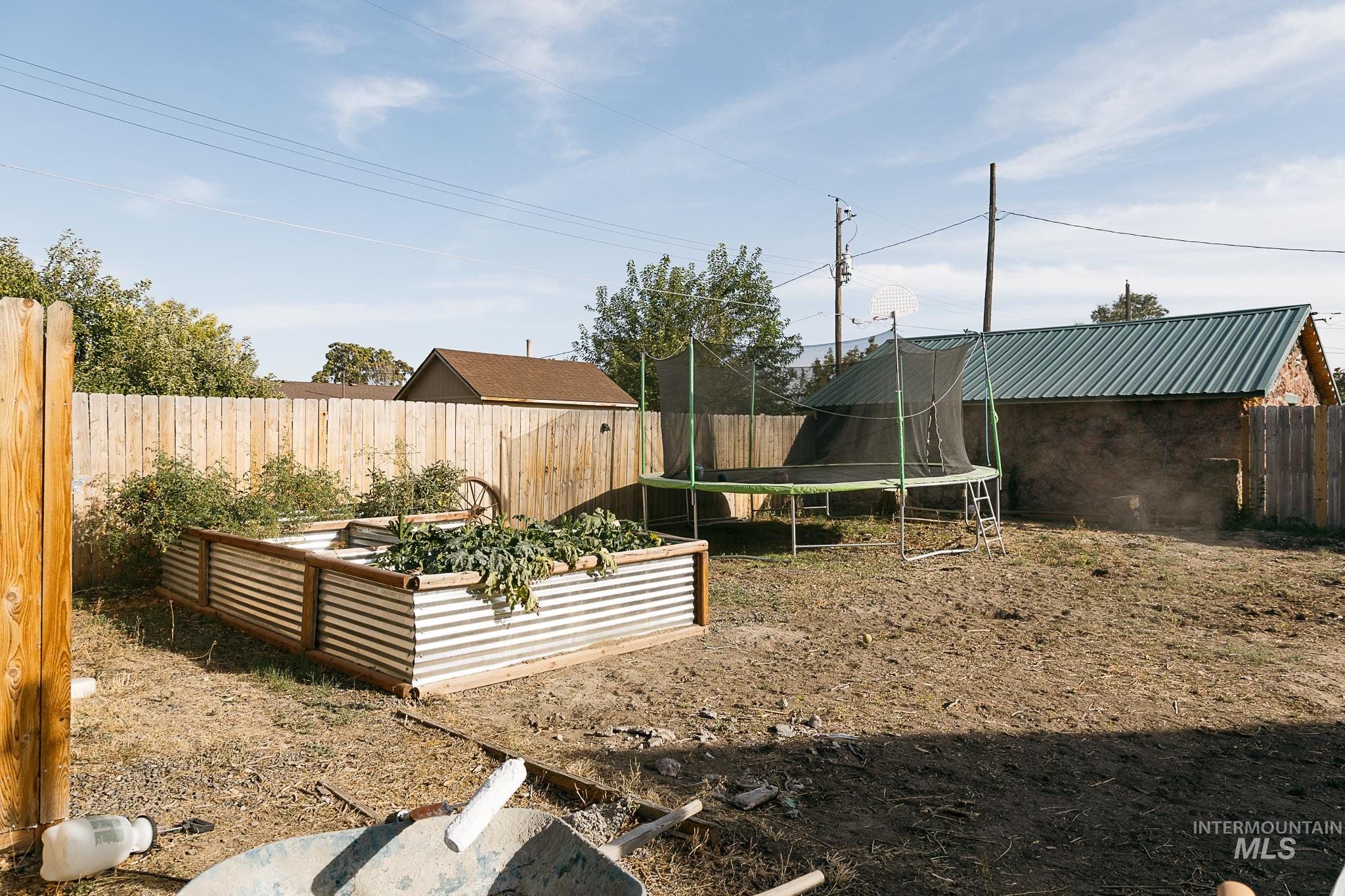 Fenced backyard featuring a trampoline and a garden