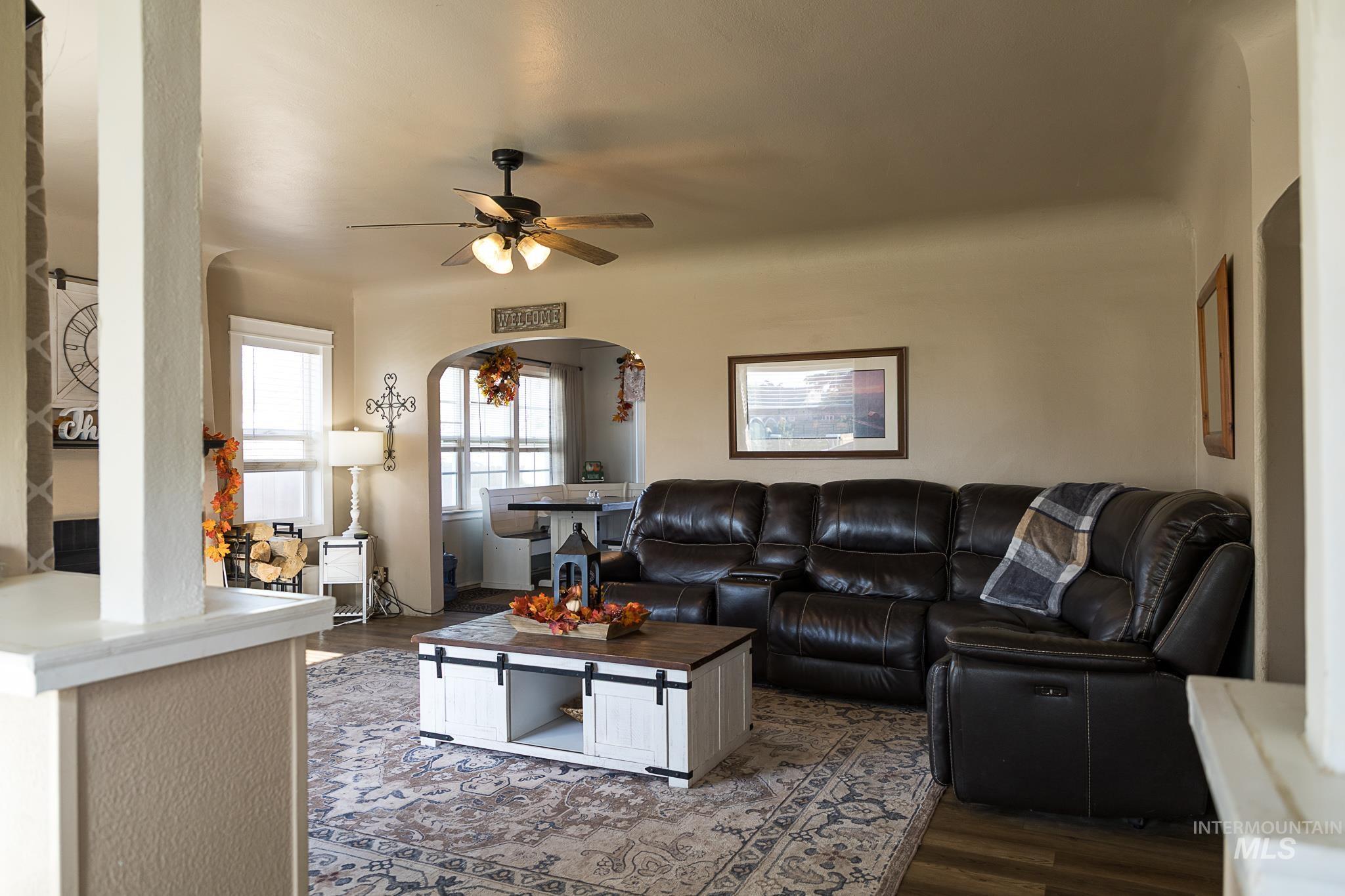 Living area with arched walkways, dark wood-type flooring, and ceiling fan