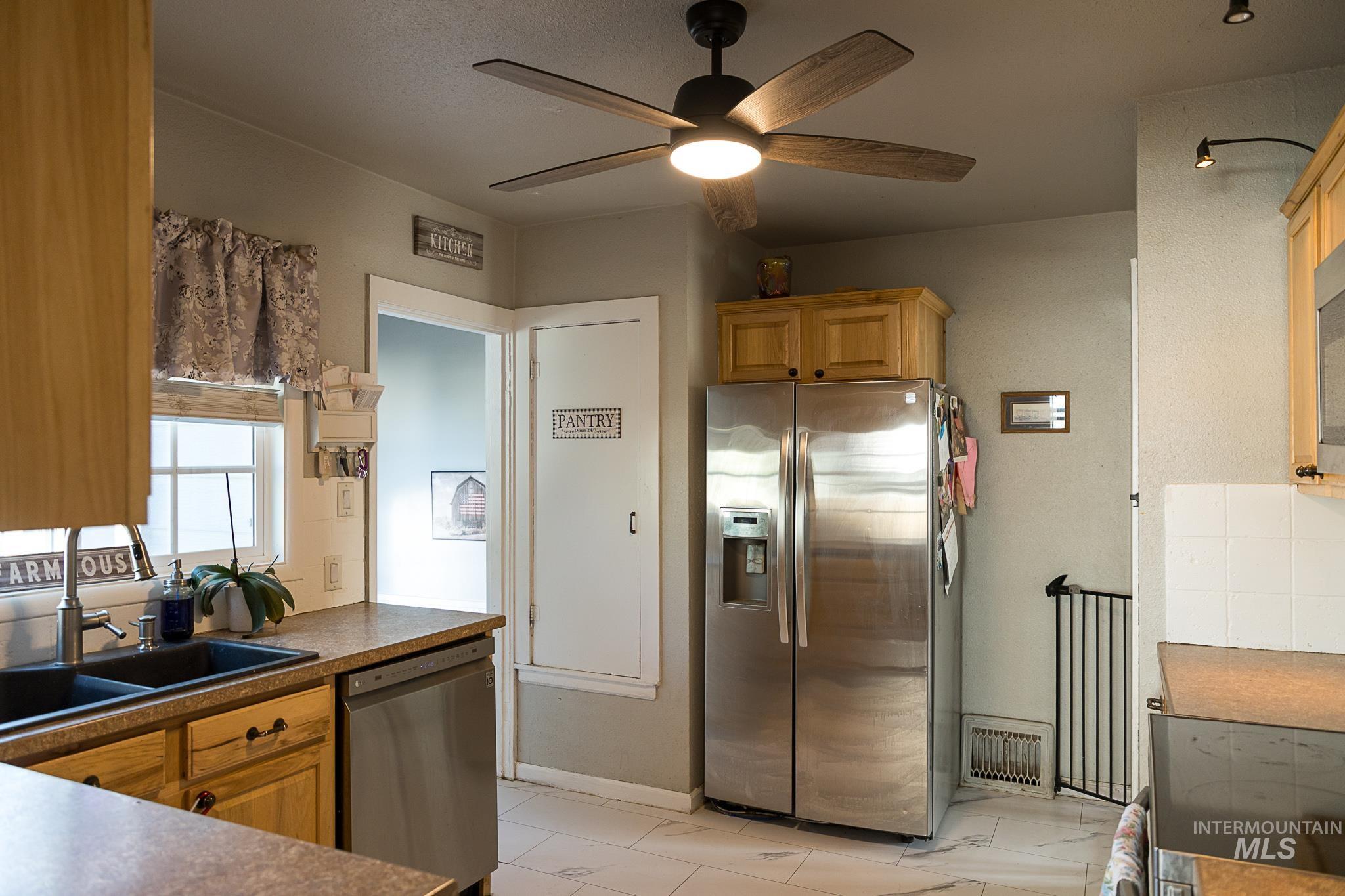 Kitchen featuring appliances with stainless steel finishes, ceiling fan, light marble finish floors, and dark countertops