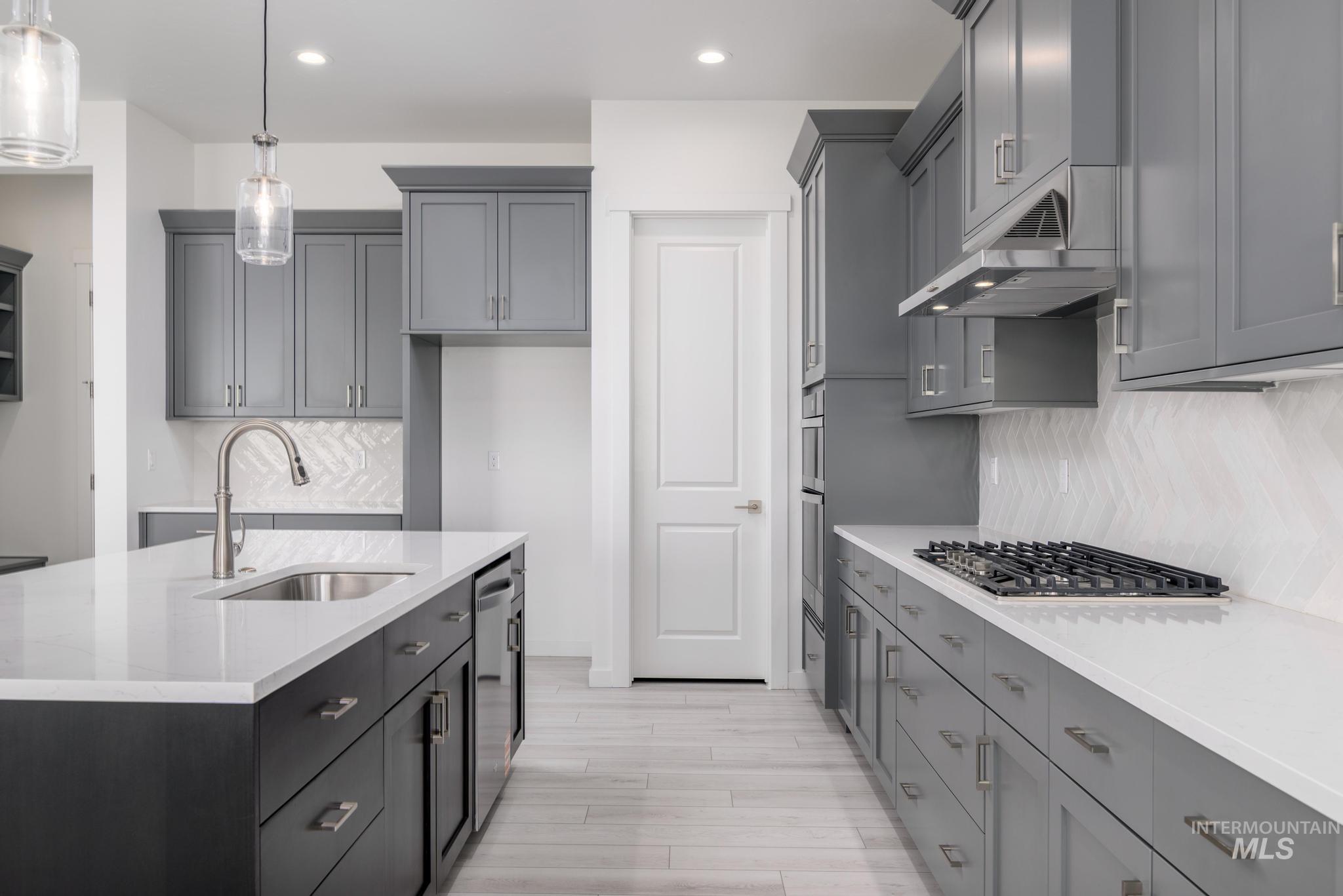 Kitchen featuring light stone counters, backsplash, hanging light fixtures, gray cabinetry, and recessed lighting