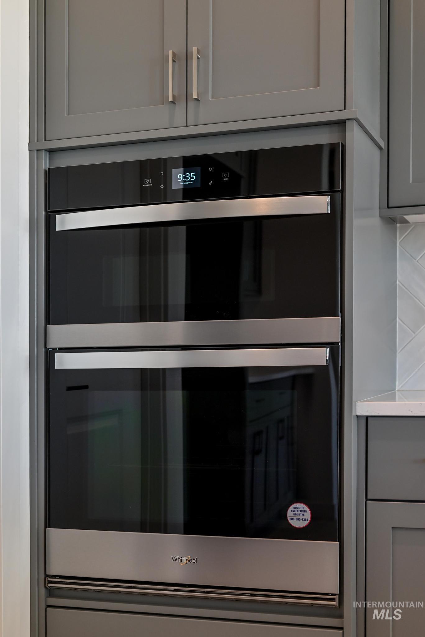 Kitchen view of gray cabinets, double oven, and light countertops
