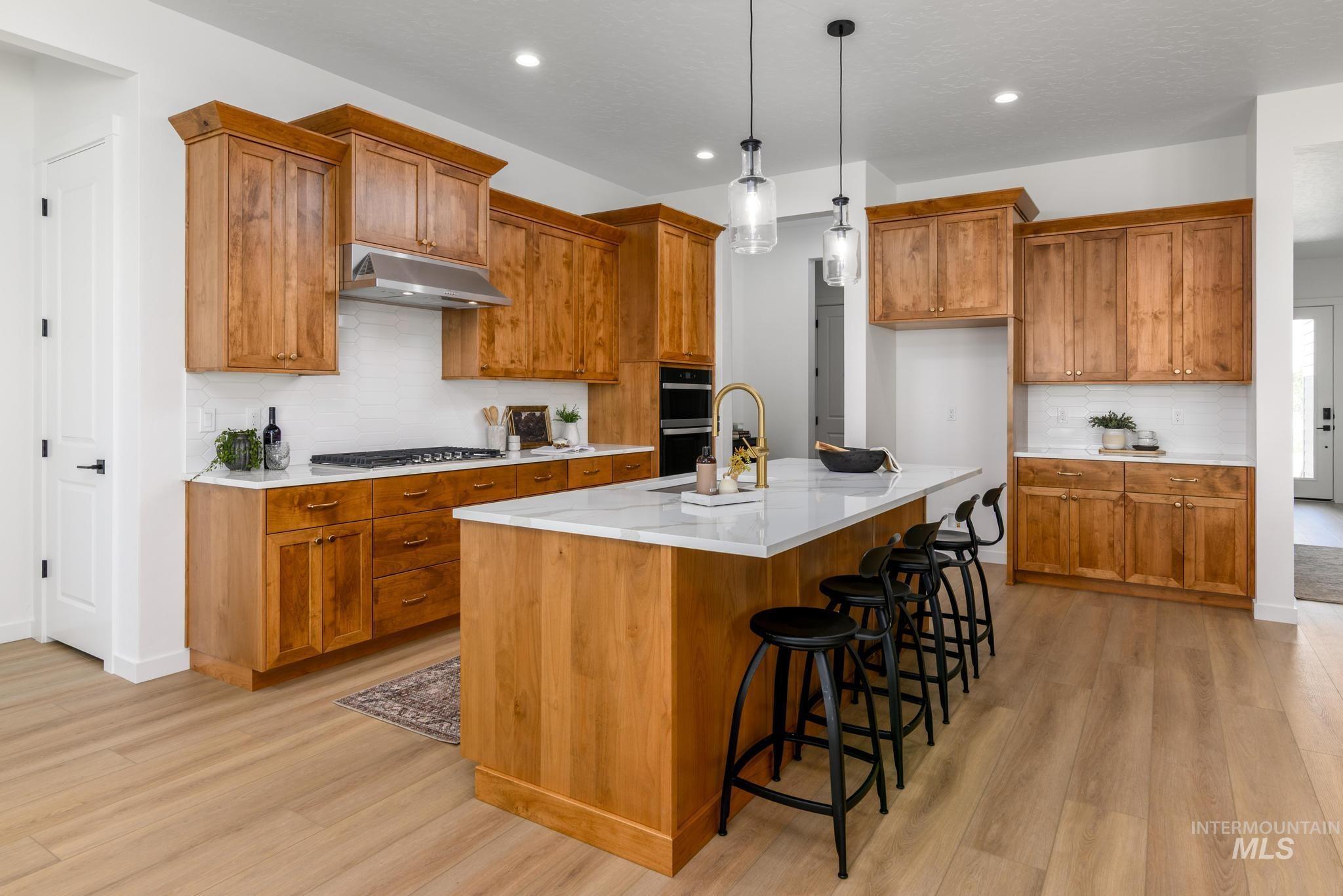 Kitchen featuring backsplash, brown cabinetry, a breakfast bar area, hanging light fixtures, and recessed lighting