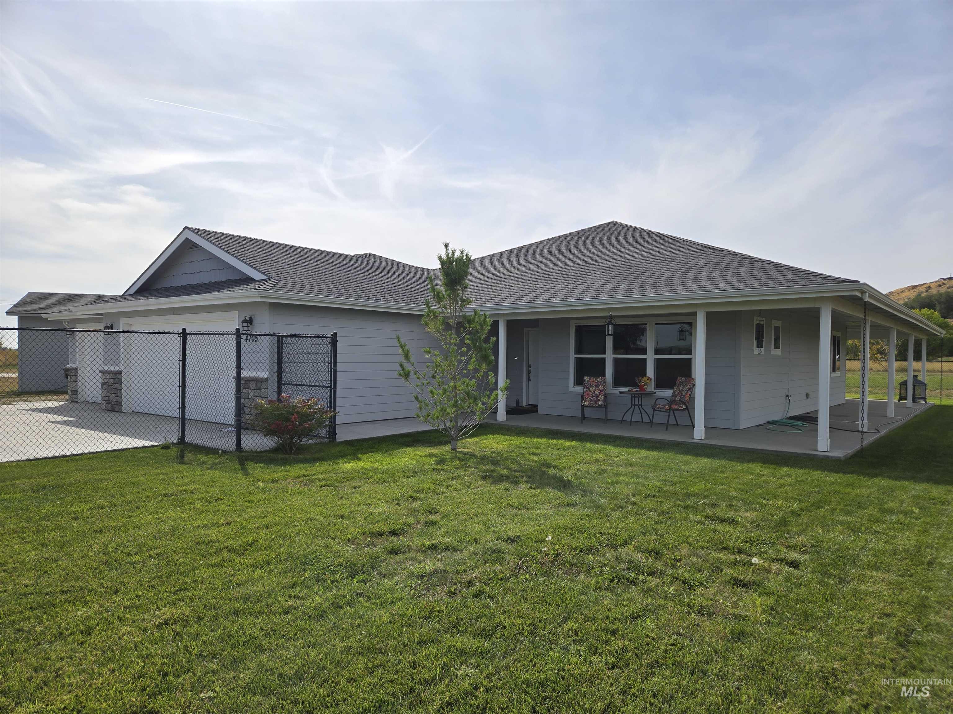 View of front of house with a shingled roof, a patio that wraps around from front along one whole side of the home to the back patio, an attached garage, and a paved driveway.