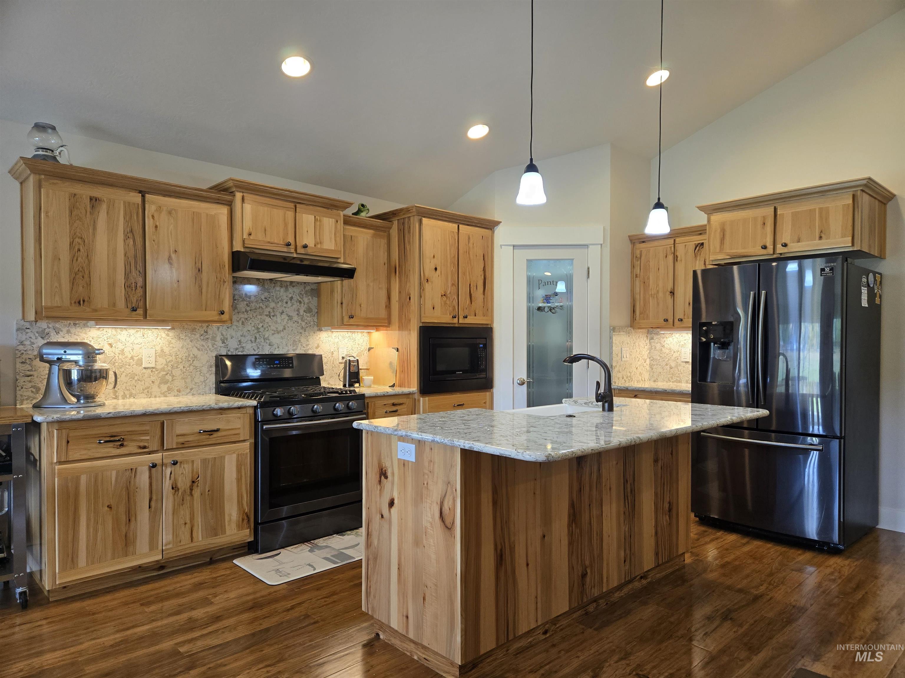Kitchen featuring decorative backsplash, black appliances, light stone countertops, vaulted ceiling, and dark wood-style floors