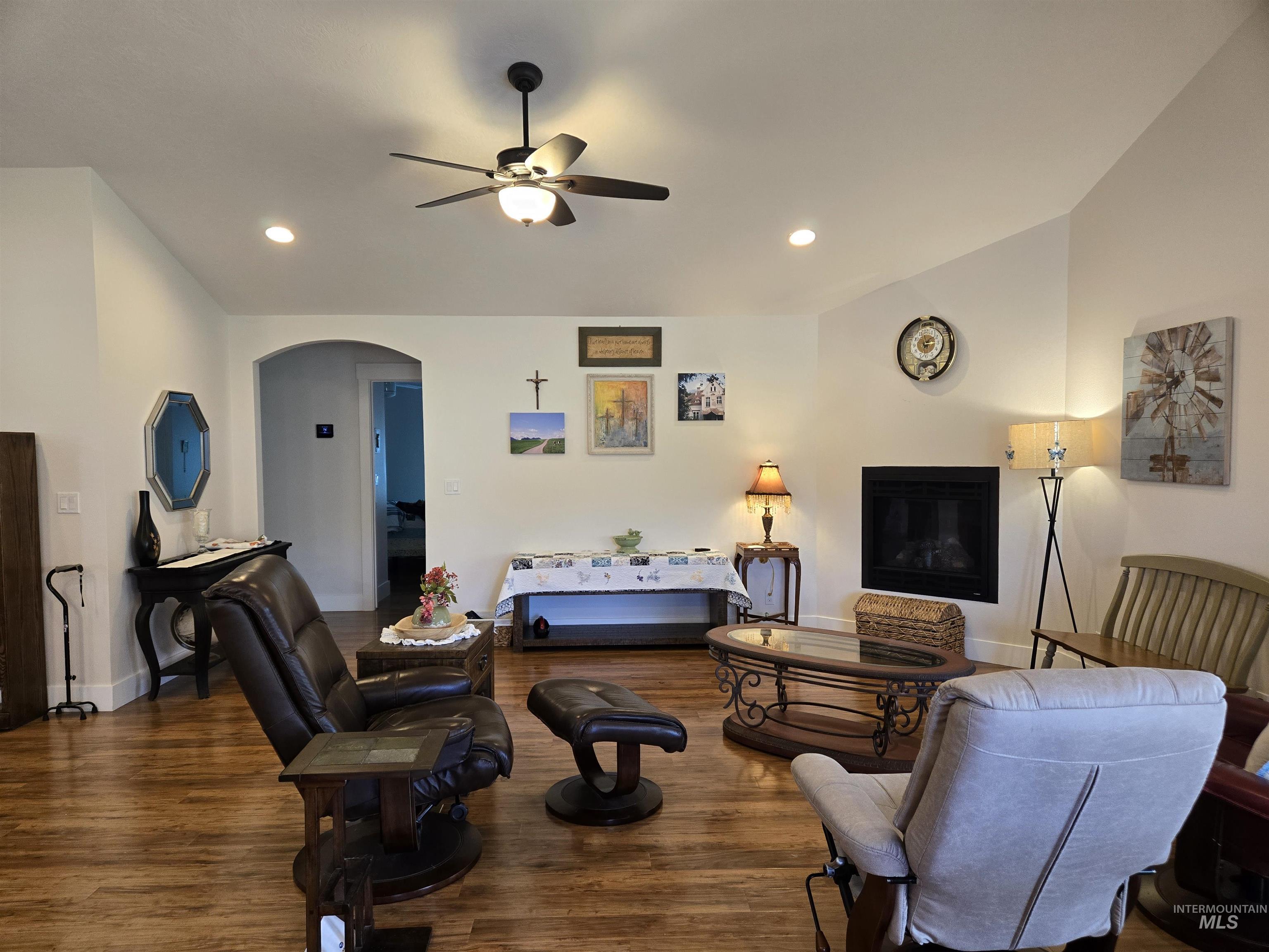 Living area with dark wood-type flooring, arched walkways, recessed lighting, ceiling fan, and a glass covered fireplace