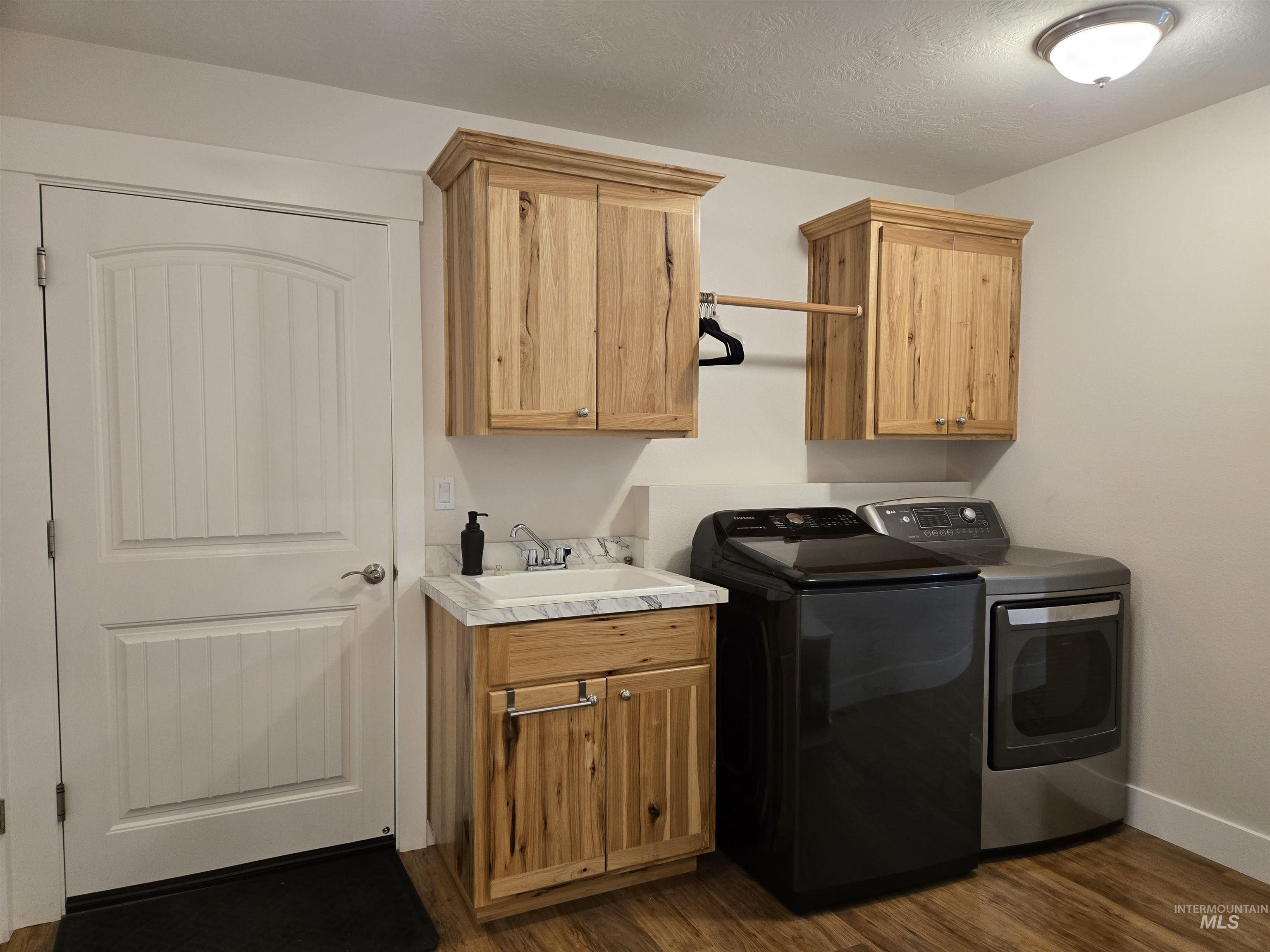 Laundry room featuring dark wood-style flooring, washer and clothes dryer, a textured ceiling, and cabinet space