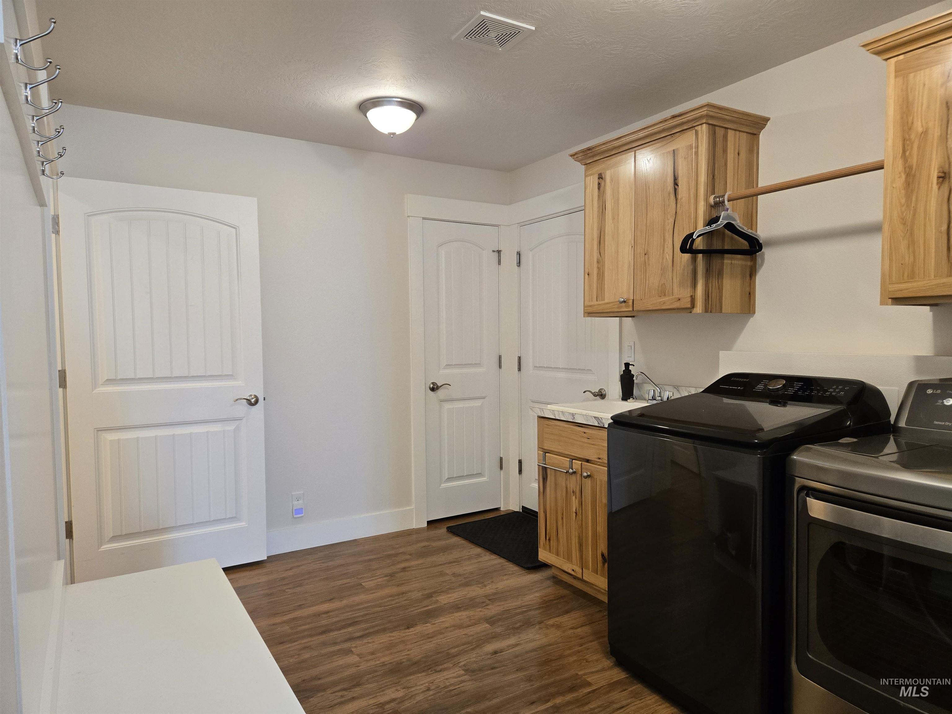 Laundry area featuring dark wood-type flooring, washing machine and dryer, a textured ceiling, and cabinet space