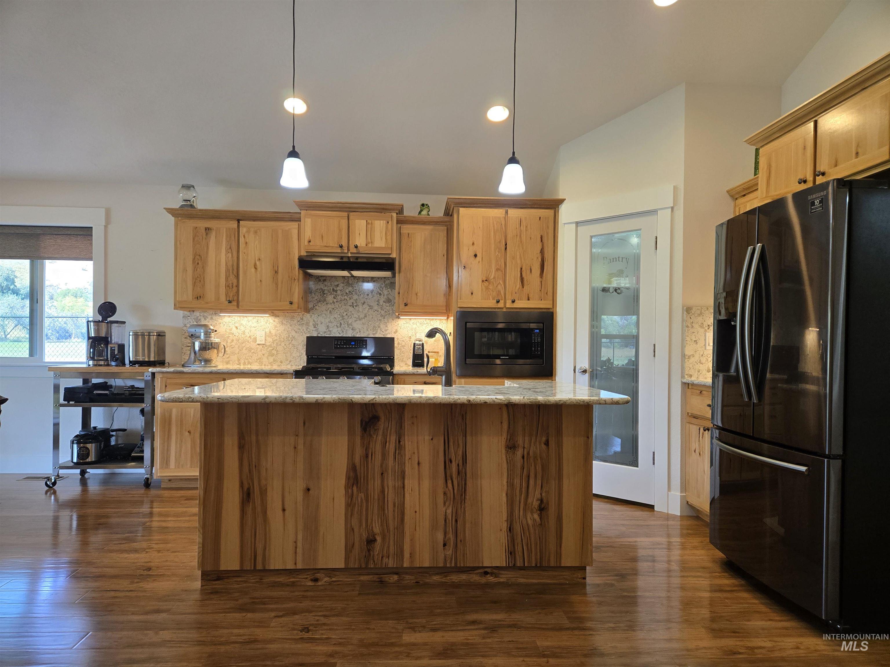 Kitchen with appliances with stainless steel finishes, decorative backsplash, an island with sink, pendant lighting, and dark wood-style floors