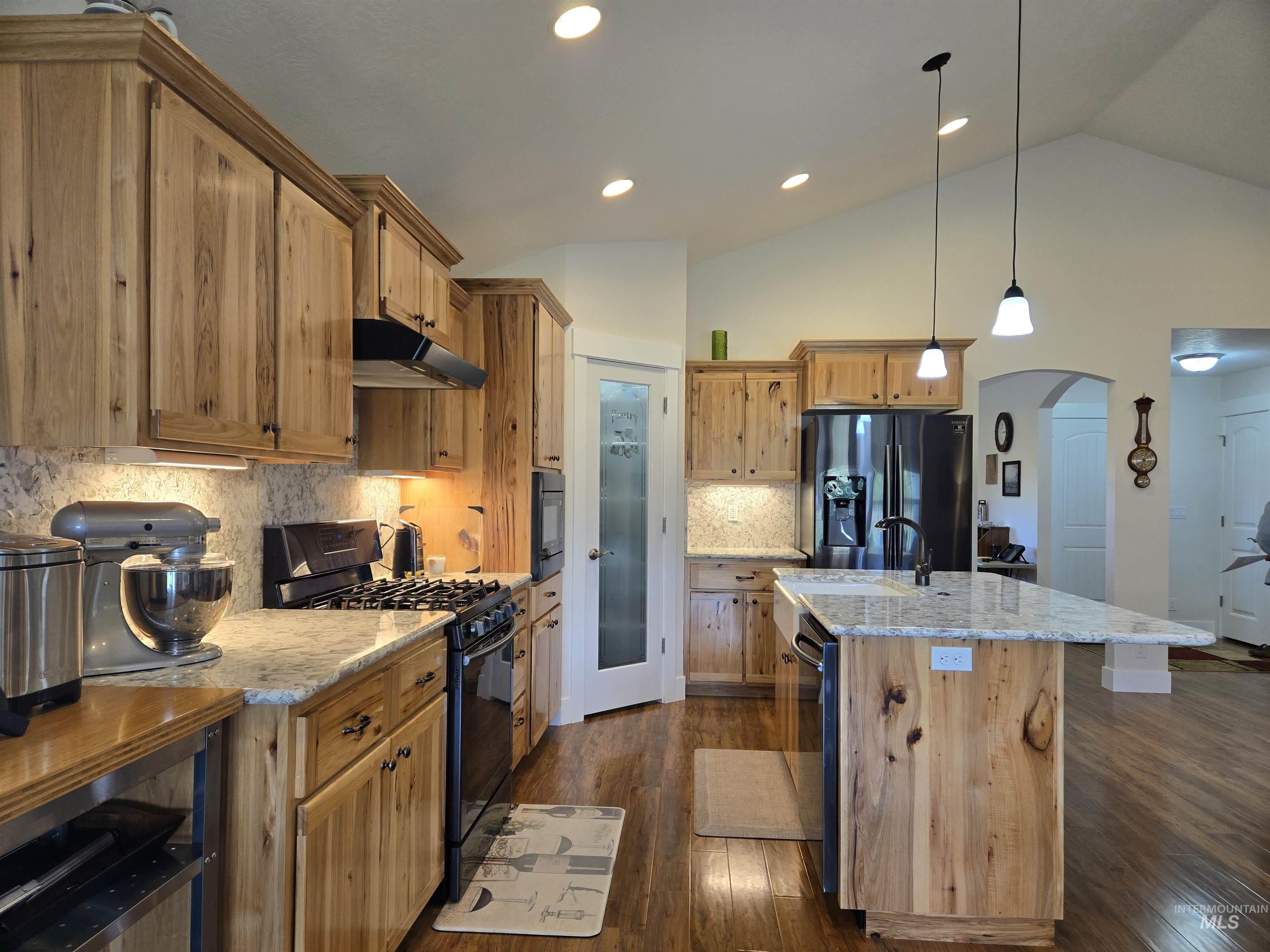 Kitchen with arched walkways, black appliances, lofted ceiling, pendant lighting, and a center island with sink