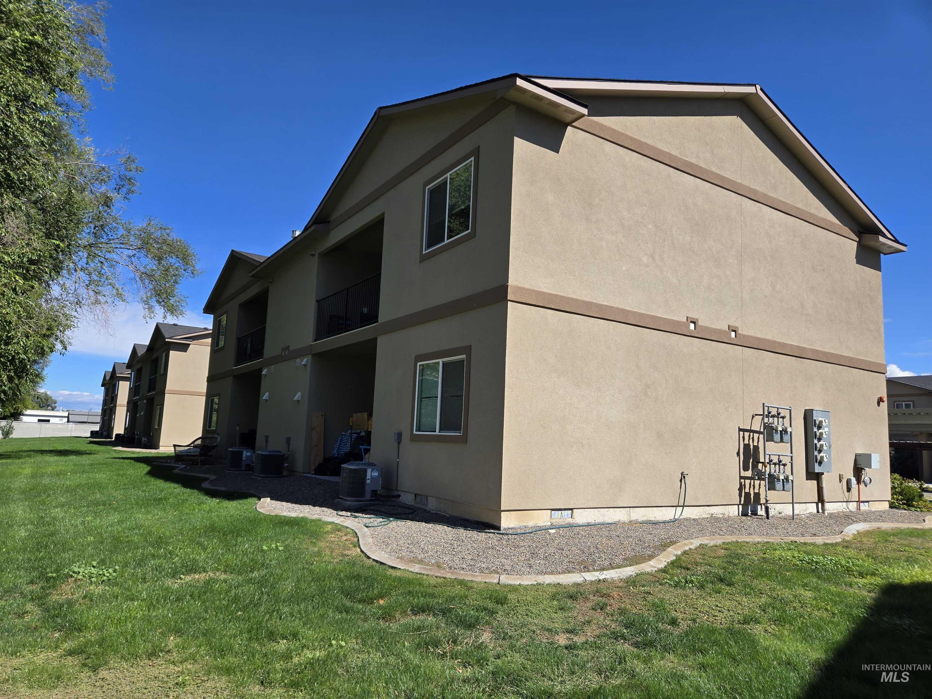 View of side of property featuring a lawn, stucco siding, and a balcony