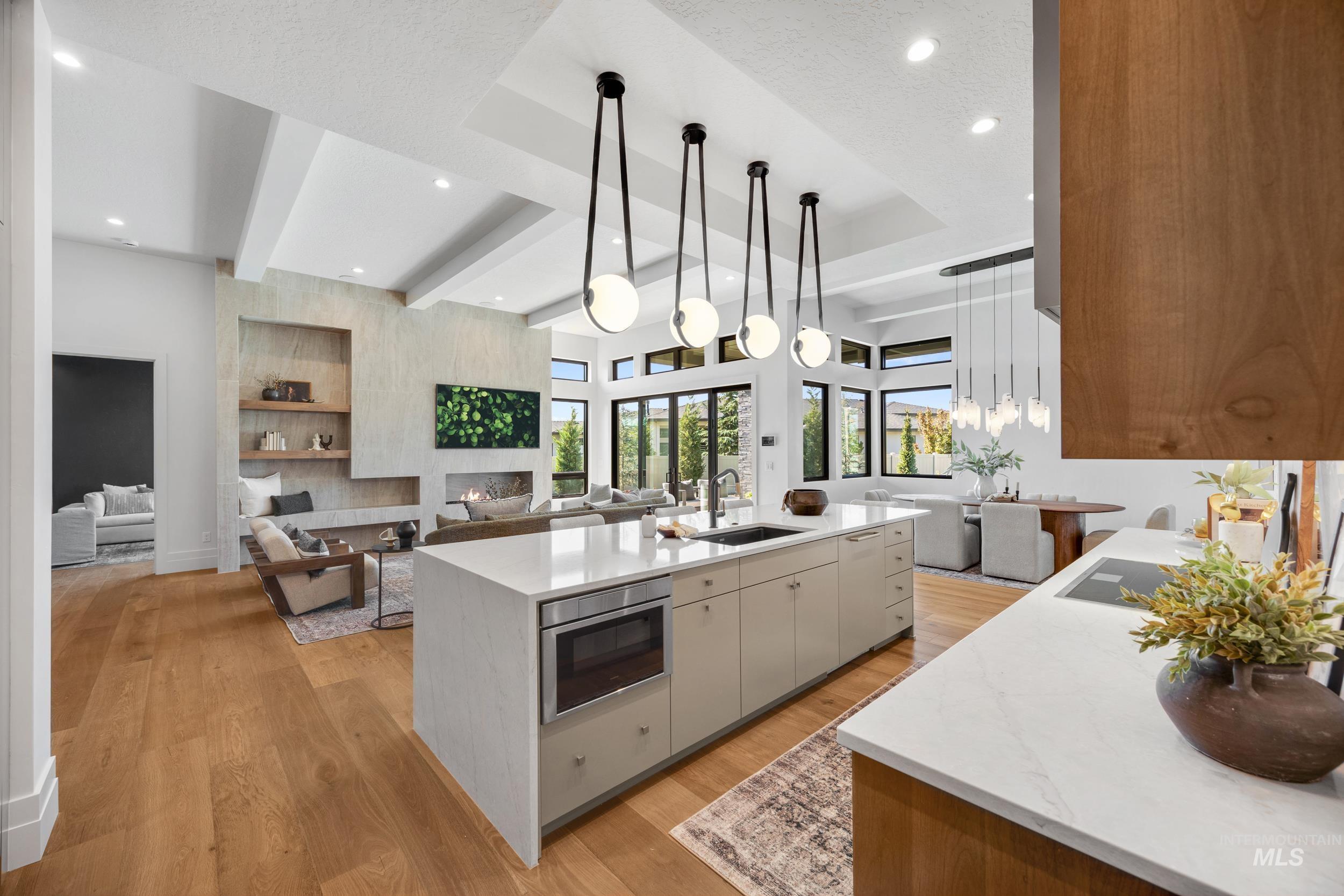 Kitchen featuring open floor plan, light stone countertops, pendant lighting, light wood-style flooring, and beam ceiling