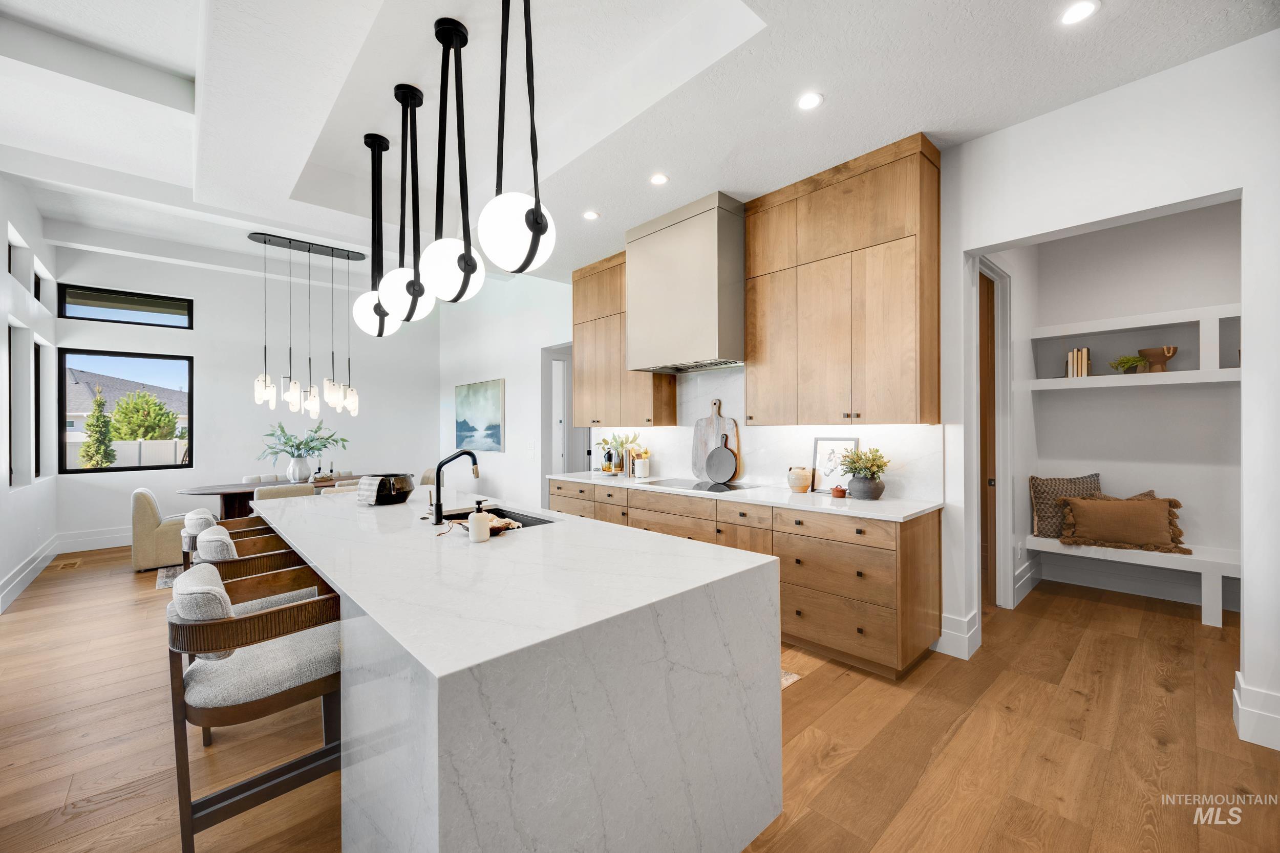 Kitchen with decorative light fixtures, a breakfast bar, light stone countertops, a large island with sink, and light wood finished floors