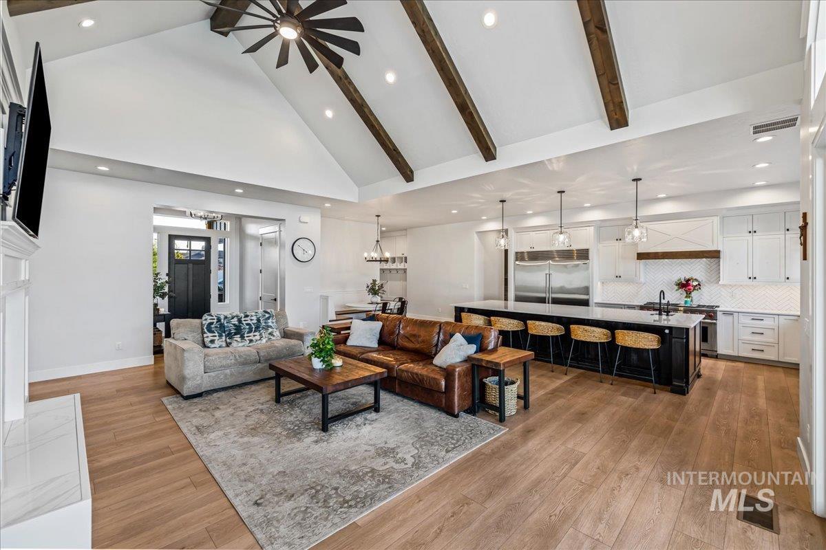 Living area with beam ceiling, high vaulted ceiling, recessed lighting, light wood-type flooring, and ceiling fan
