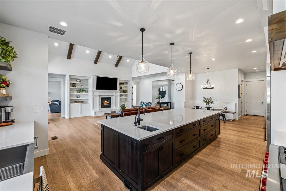 Kitchen with dark brown cabinets, a glass covered fireplace, light wood finished floors, open floor plan, and recessed lighting