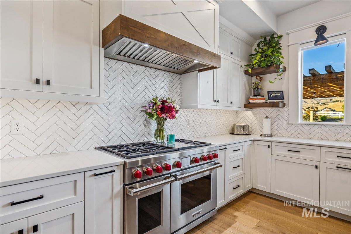 Kitchen featuring white cabinetry, range with two ovens, custom range hood, light wood-type flooring, and backsplash
