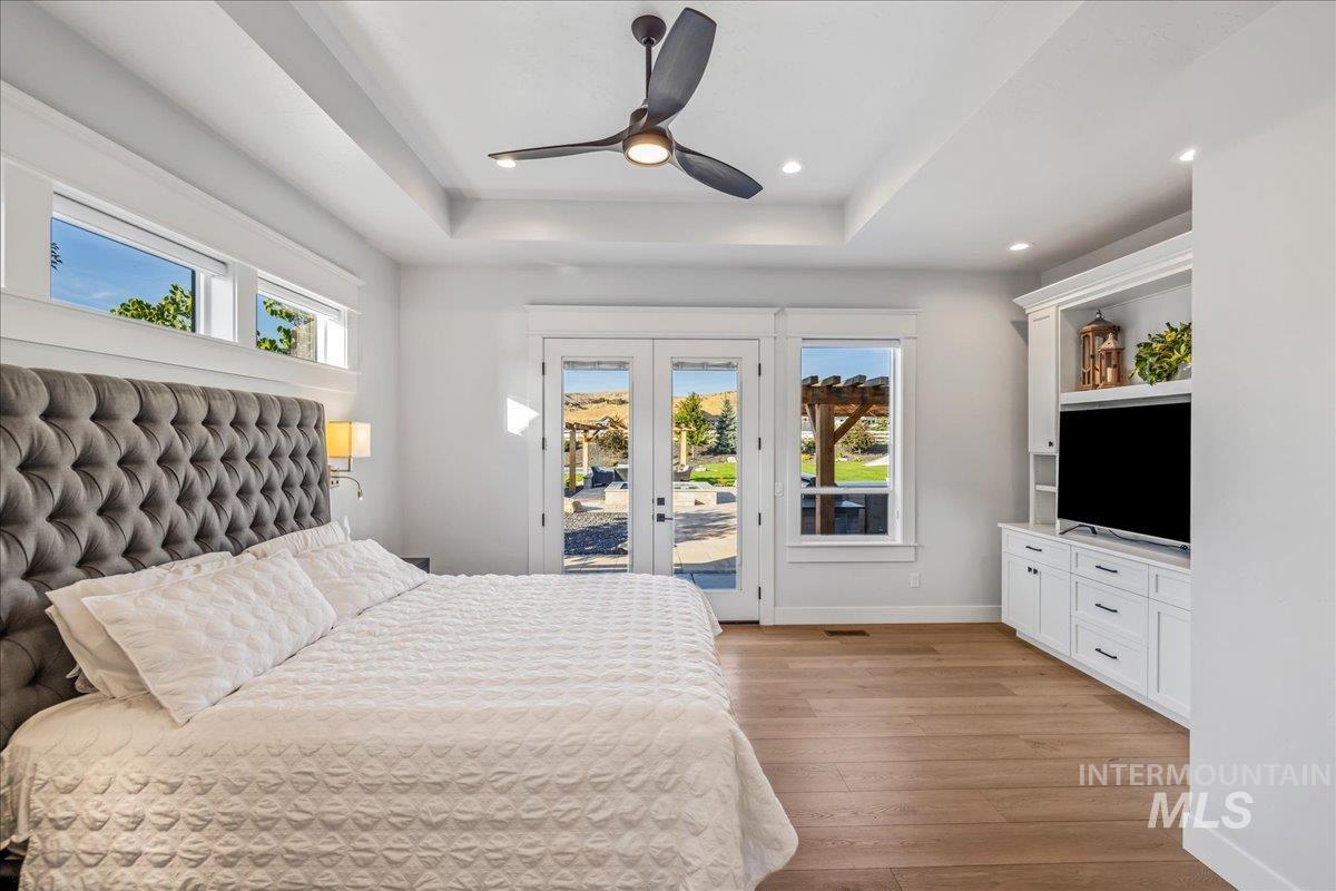 Bedroom featuring french doors, light wood-style flooring, access to exterior, a raised ceiling, and ceiling fan