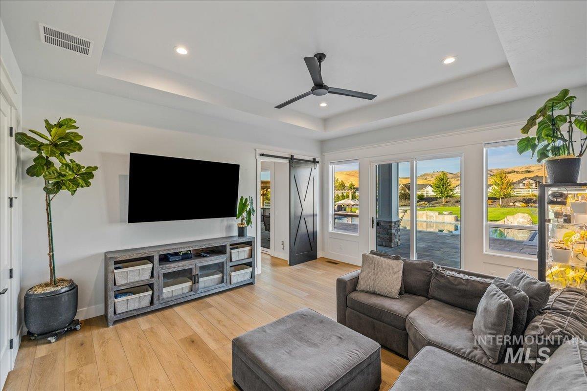 Living room featuring a barn door, a tray ceiling, light wood-type flooring, recessed lighting, and ceiling fan