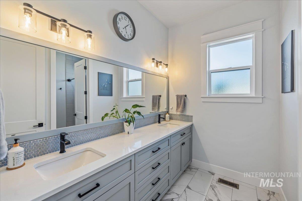 Full bath featuring double vanity, light marble finish floors, and a tile shower