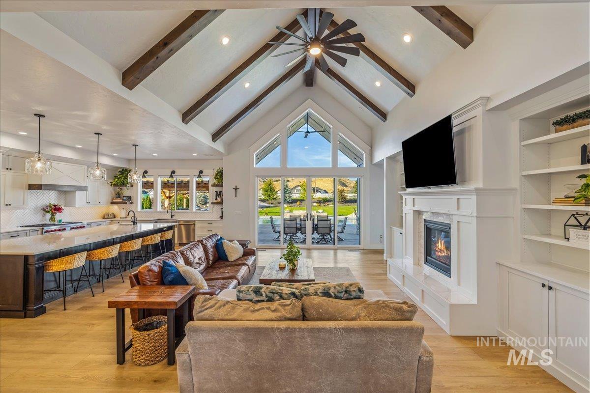 Living room featuring beamed ceiling, high vaulted ceiling, light wood-style floors, a glass covered fireplace, and recessed lighting