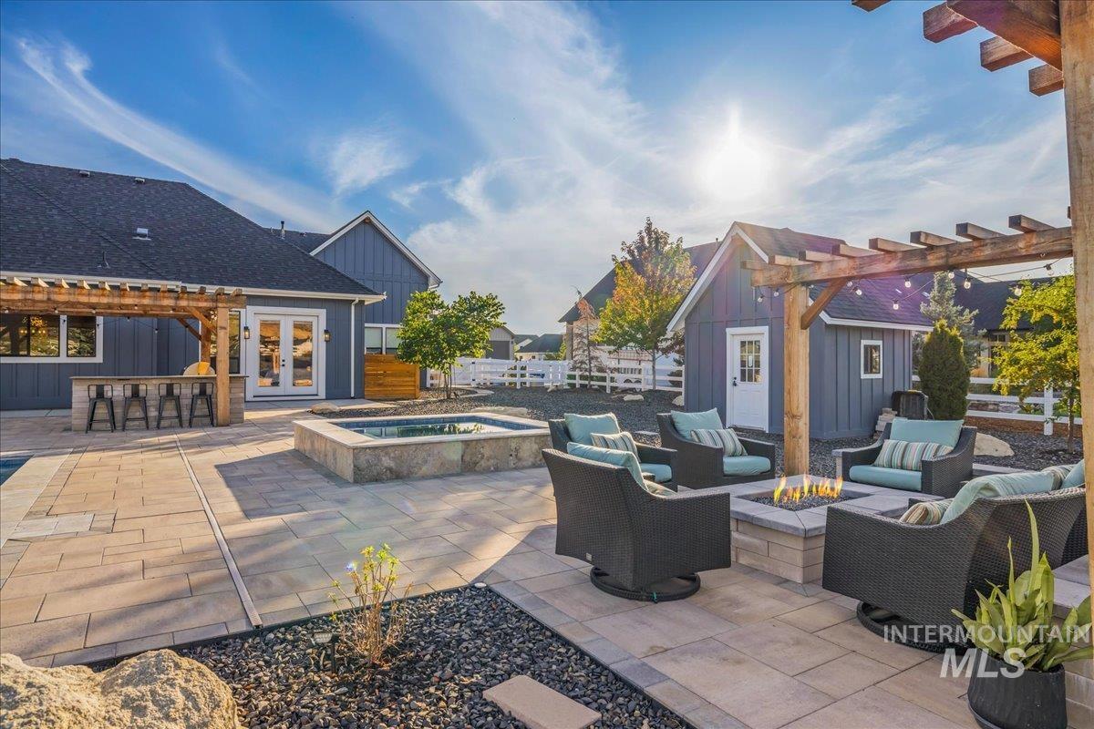 View of patio / terrace featuring a pergola, an in-ground hot tub, an outdoor living space with a fire pit, an outdoor structure, and french doors