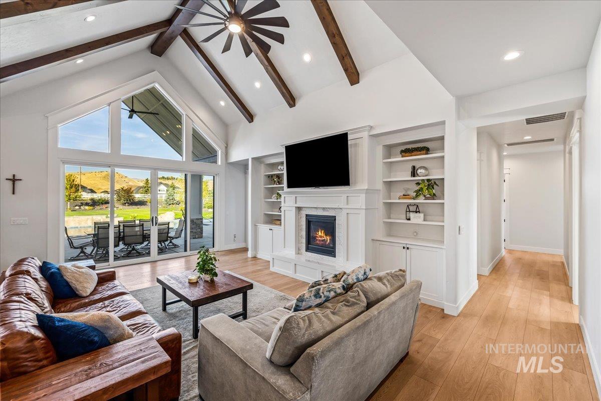 Living area featuring high vaulted ceiling, light wood-style flooring, beamed ceiling, a premium fireplace, and recessed lighting