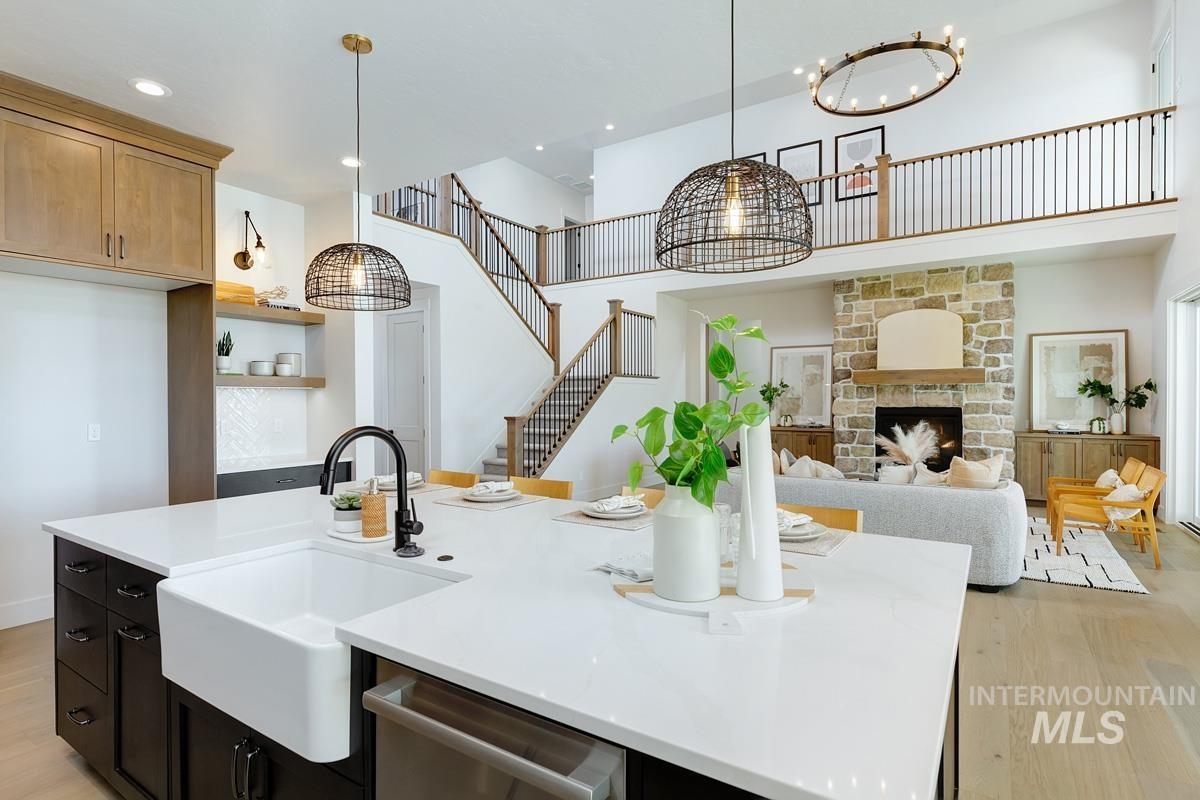 Kitchen featuring light wood-style floors, a fireplace, decorative light fixtures, a towering ceiling, and a kitchen island with sink