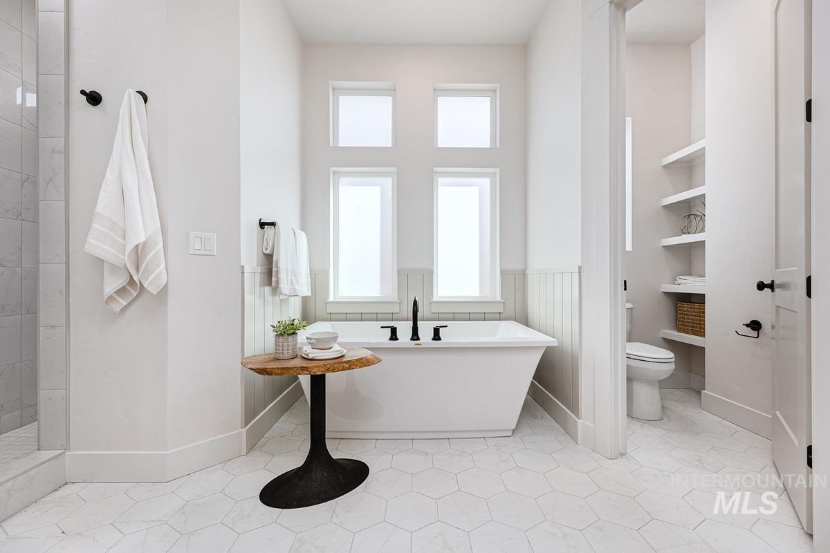 Bathroom featuring a freestanding tub, a tile shower, light tile patterned floors, and a wainscoted wall