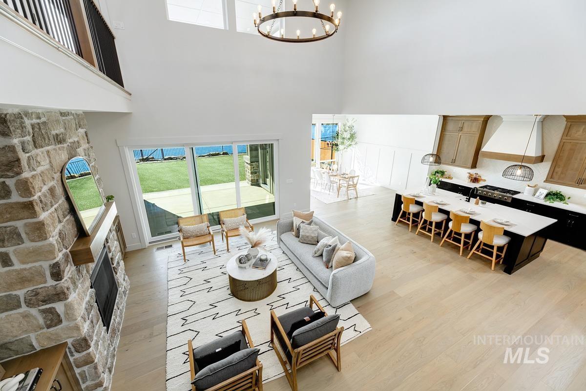 Living room featuring a fireplace, healthy amount of natural light, a chandelier, light wood-style floors, and a high ceiling