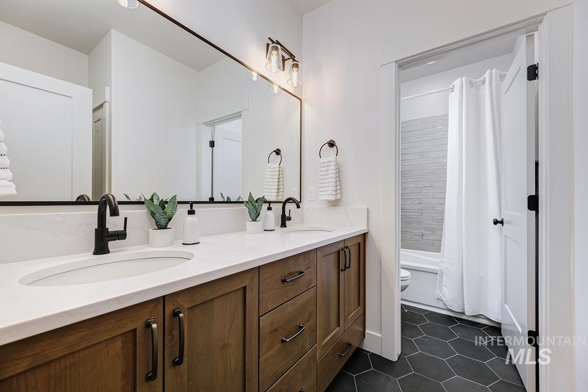 Bathroom featuring dark tile patterned floors, shower / bath combination with curtain, and double vanity
