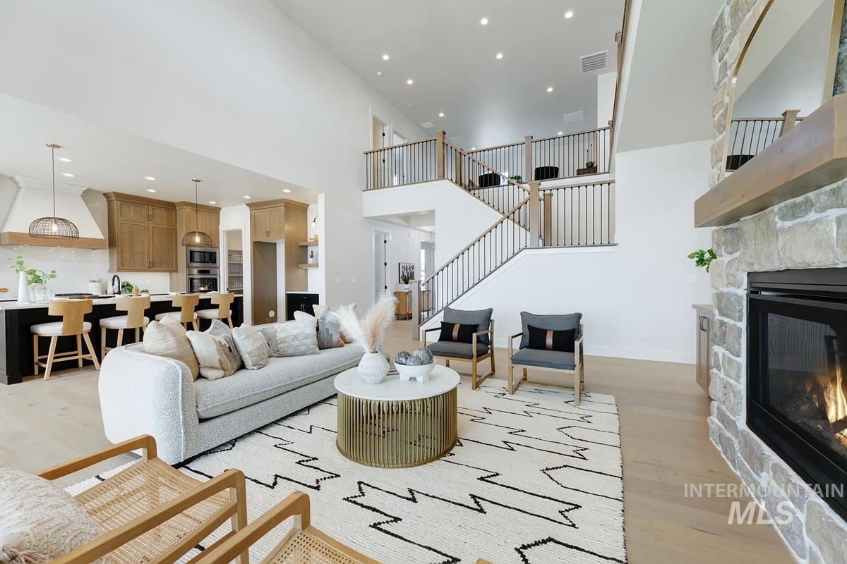 Living area featuring light wood-style floors, a high ceiling, recessed lighting, a stone fireplace, and stairway