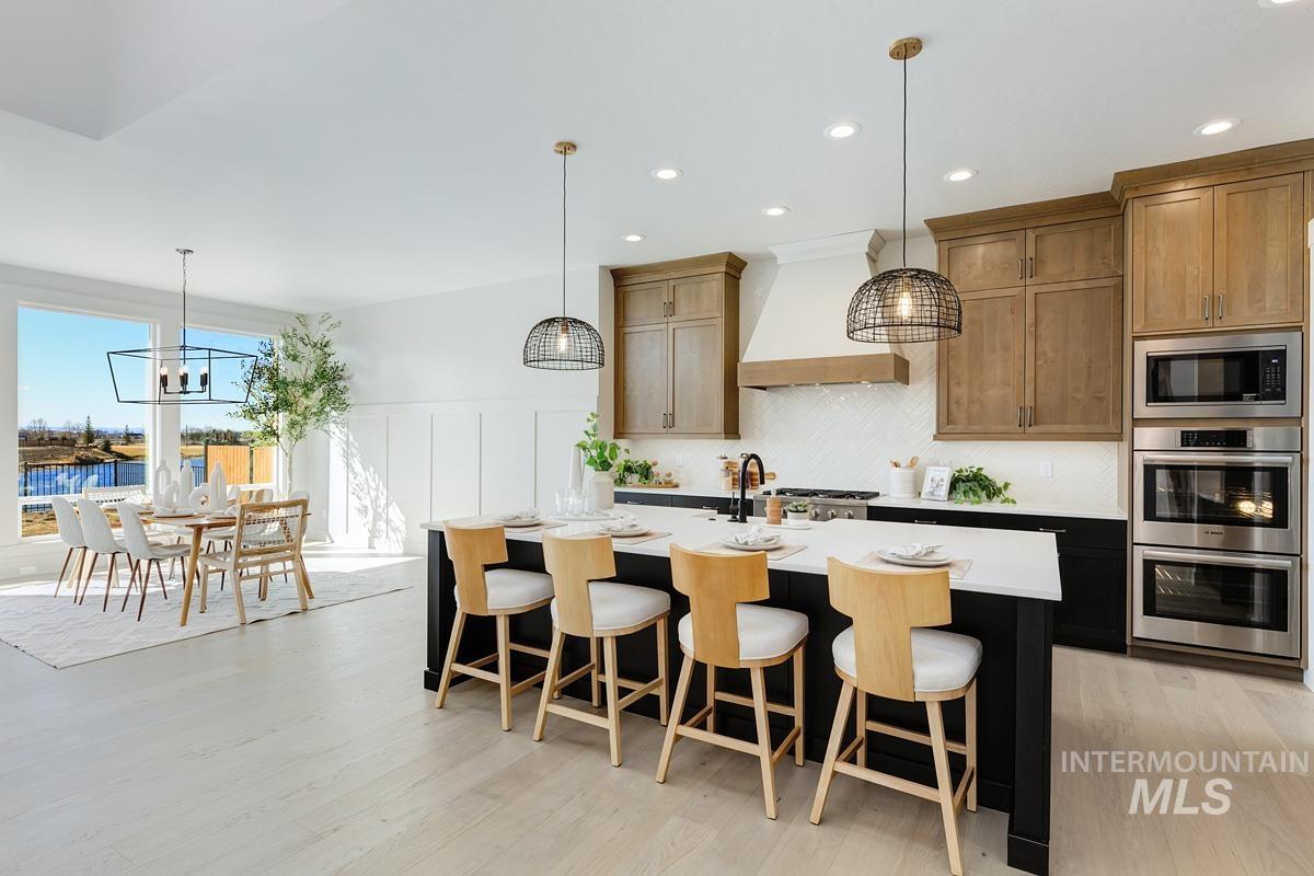 Kitchen featuring a kitchen breakfast bar, decorative light fixtures, appliances with stainless steel finishes, backsplash, and a kitchen island with sink