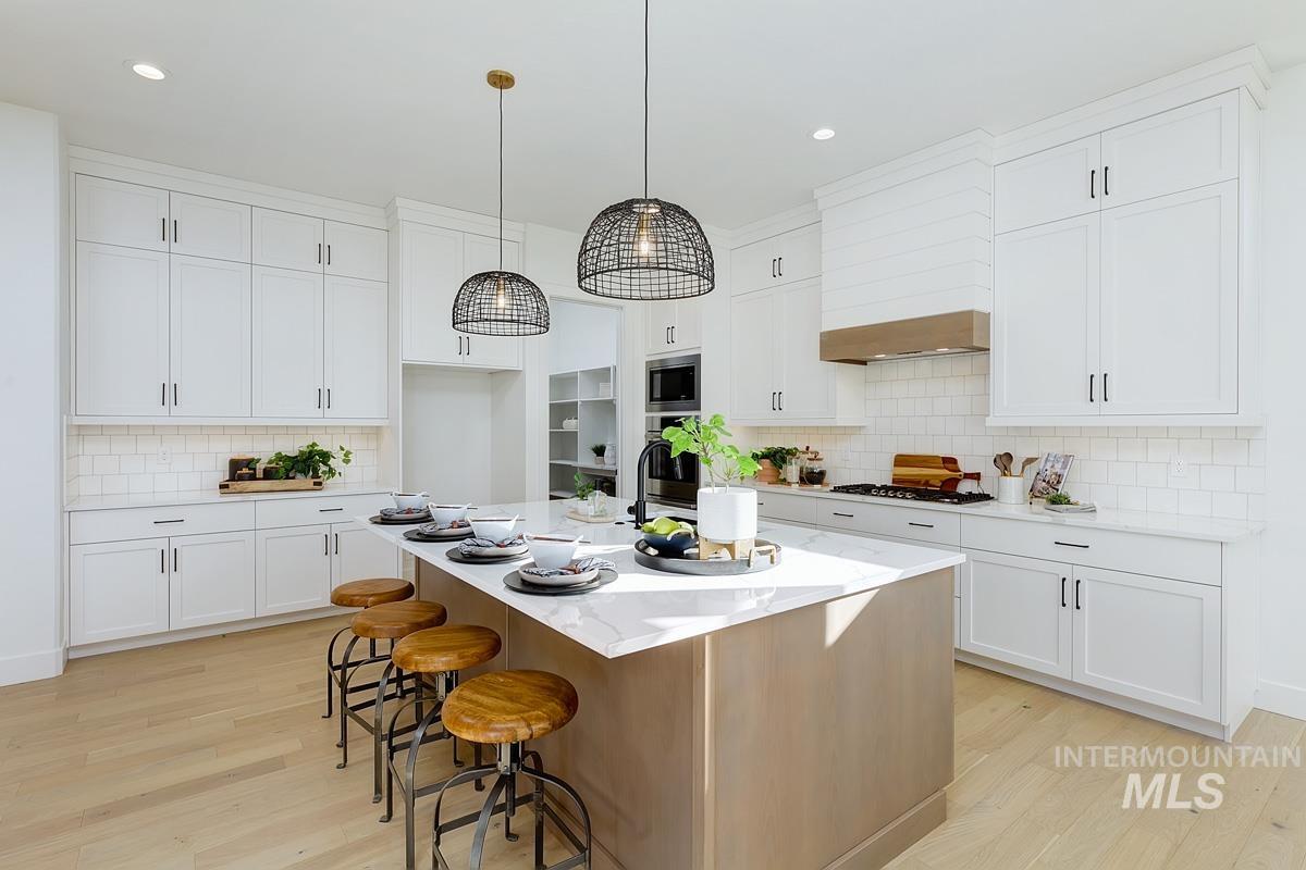 Kitchen with decorative backsplash, decorative light fixtures, a kitchen breakfast bar, light wood finished floors, and recessed lighting