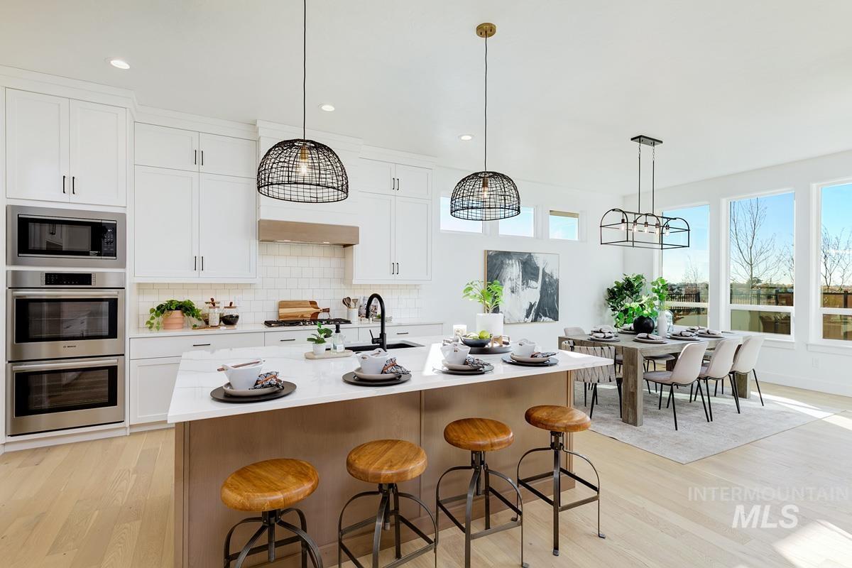 Kitchen with light wood finished floors, a breakfast bar, tasteful backsplash, decorative light fixtures, and white cabinets