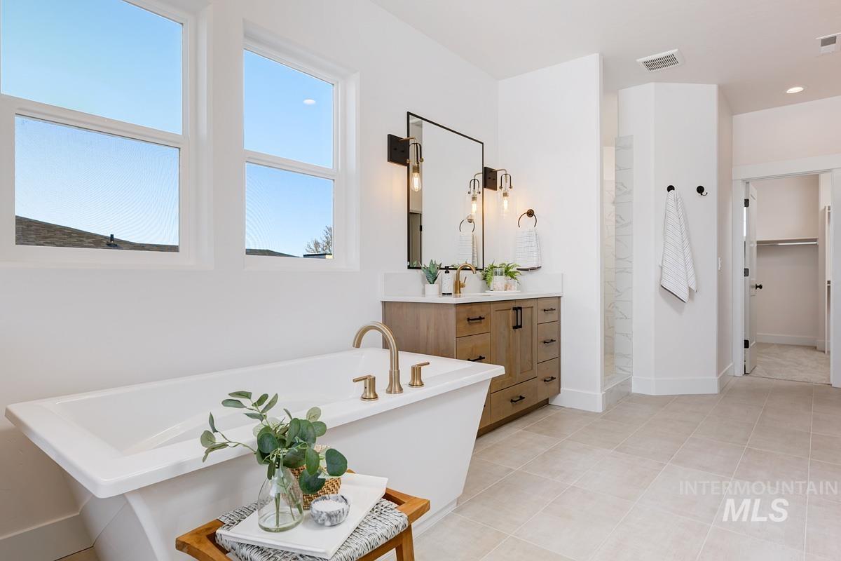 Bathroom featuring vanity, a soaking tub, walk in shower, light tile patterned floors, and a walk in closet