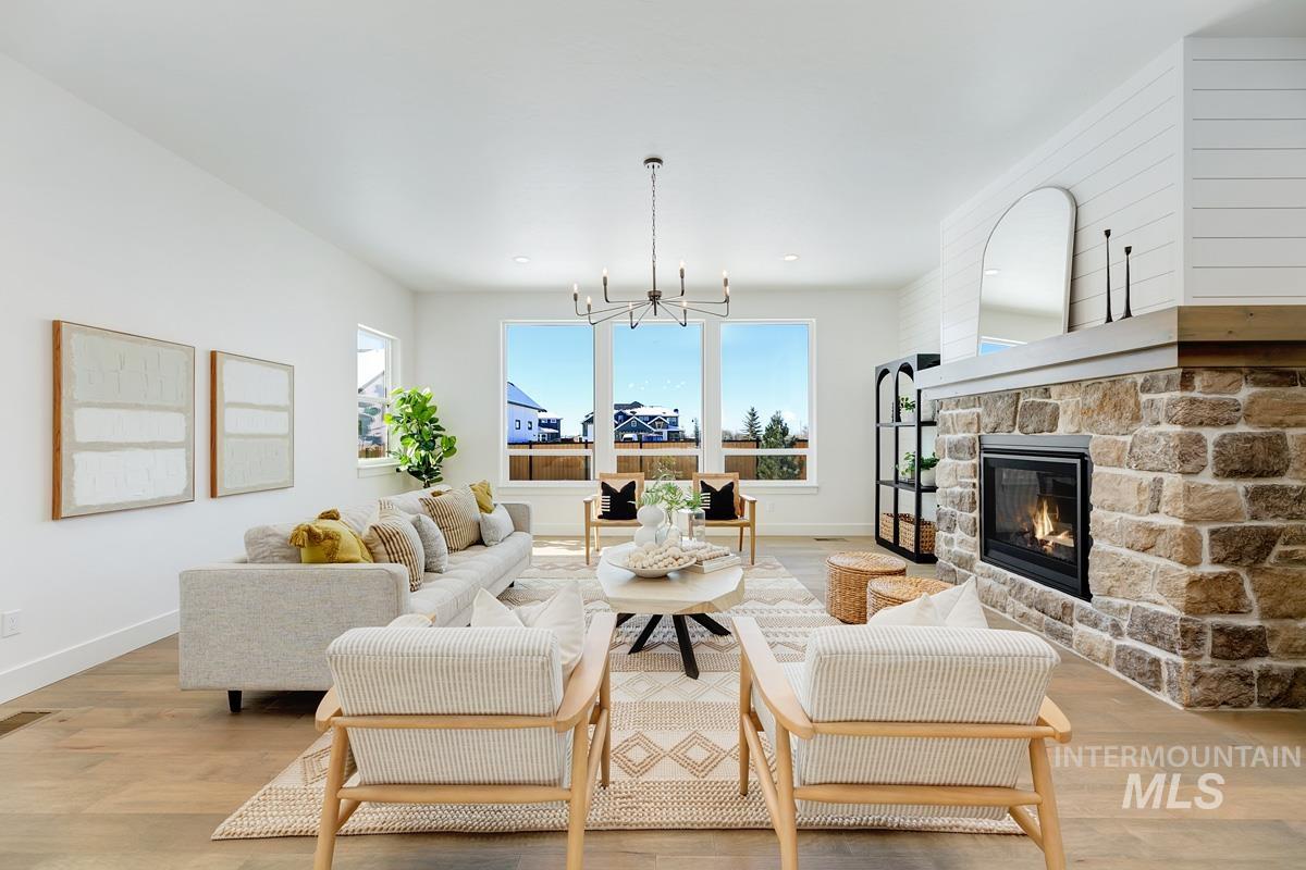 Living room featuring light wood-style flooring, a stone fireplace, and a chandelier