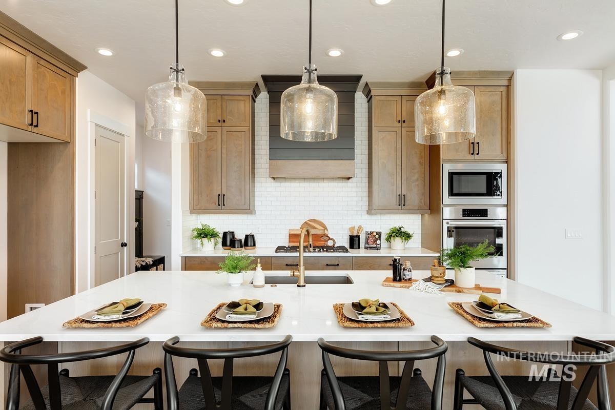 Kitchen featuring a breakfast bar area, stainless steel appliances, decorative backsplash, decorative light fixtures, and an island with sink