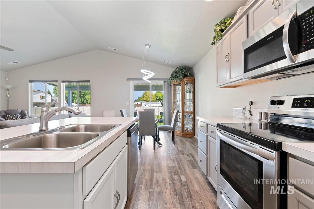 Kitchen with appliances with stainless steel finishes, light countertops, lofted ceiling, open floor plan, and light wood finished floors