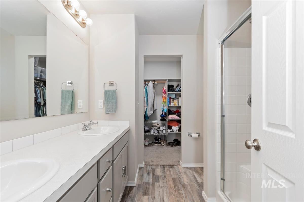 Bathroom with a stall shower, double vanity, a spacious closet, and light wood-style flooring